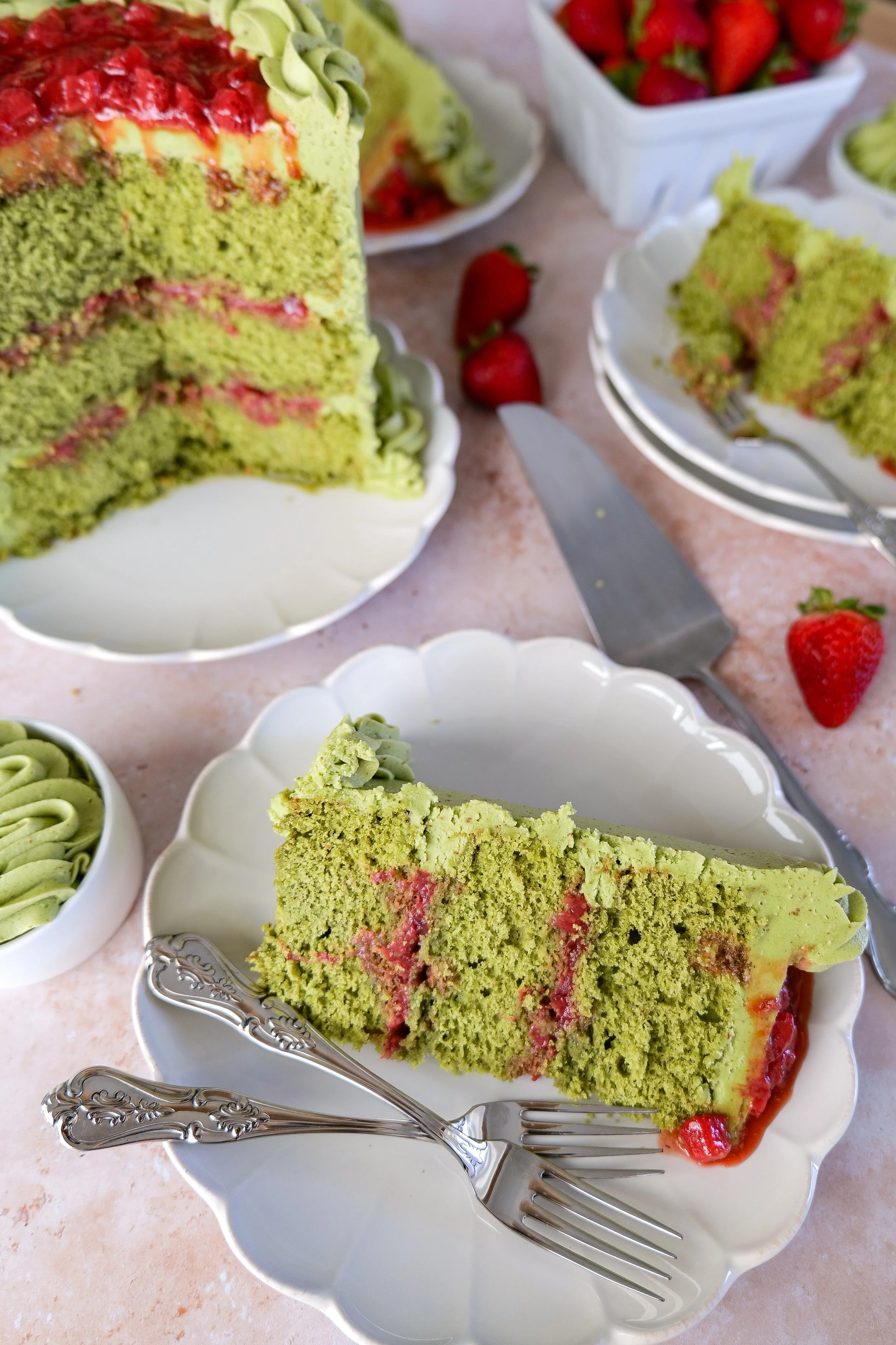 Slices of matcha strawberry cake with brown butter frosting and fresh strawberries