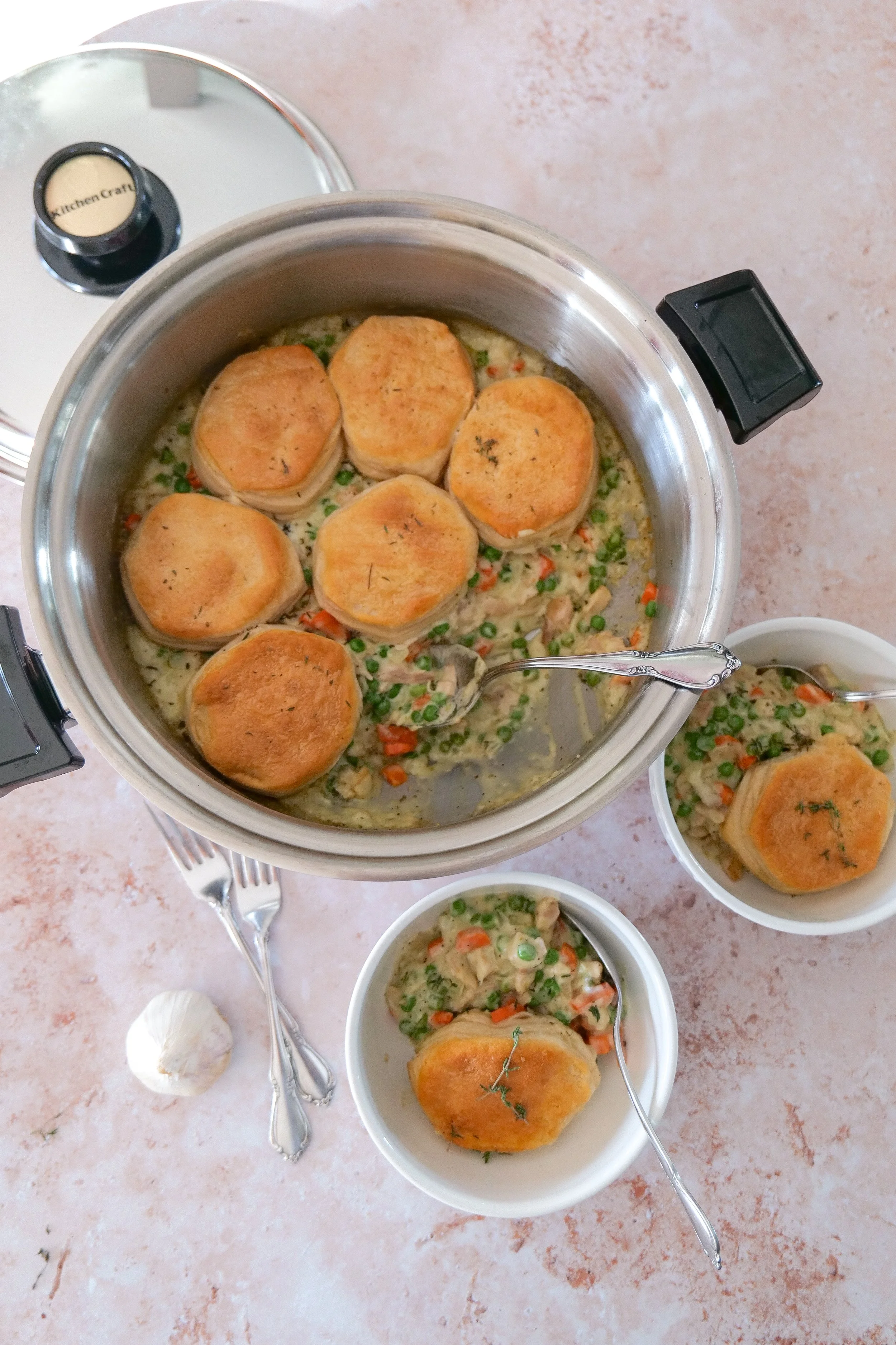 Fresh ingredients for skillet chicken pot pie including chicken, carrots, onion, garlic, peas, broth, cream, herbs, and refrigerated biscuits.