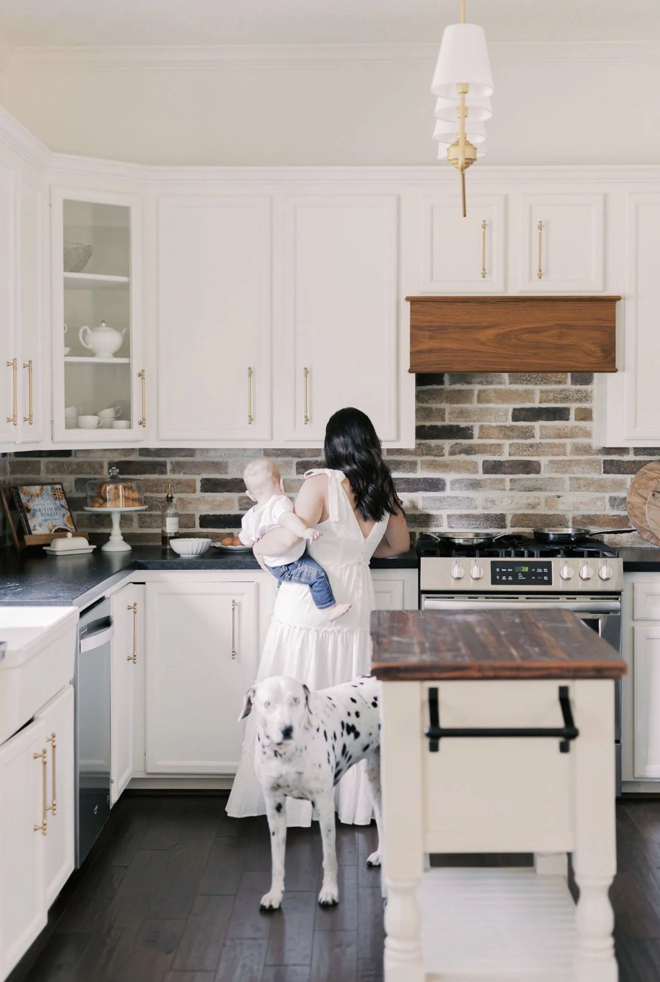 Mom holding her baby with her back to the camera as their Dalmatian walks through the kitchen of their Texas home