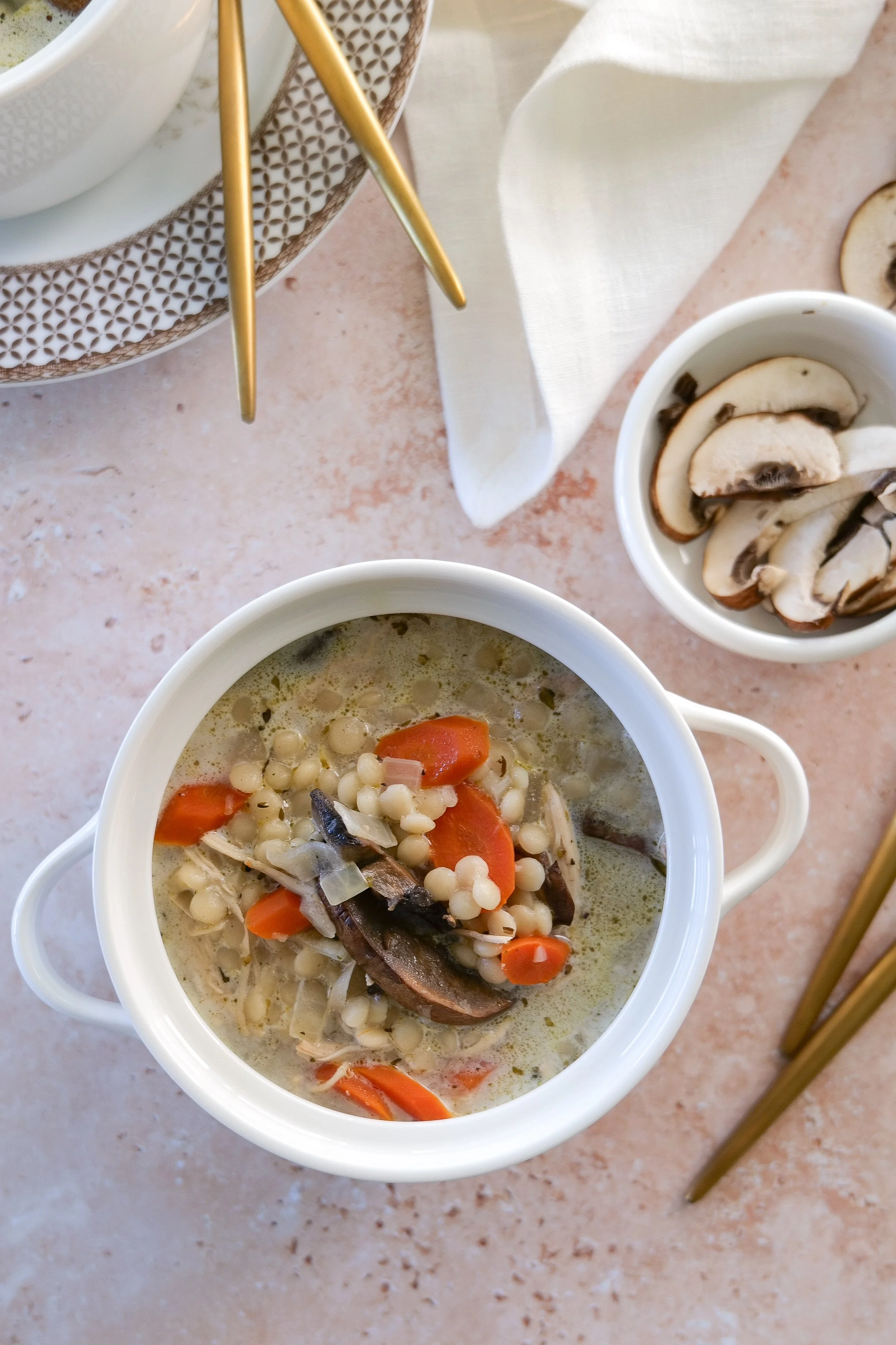 Chicken couscous soup with sliced mushrooms and carrots in a creamy seasoned broth.