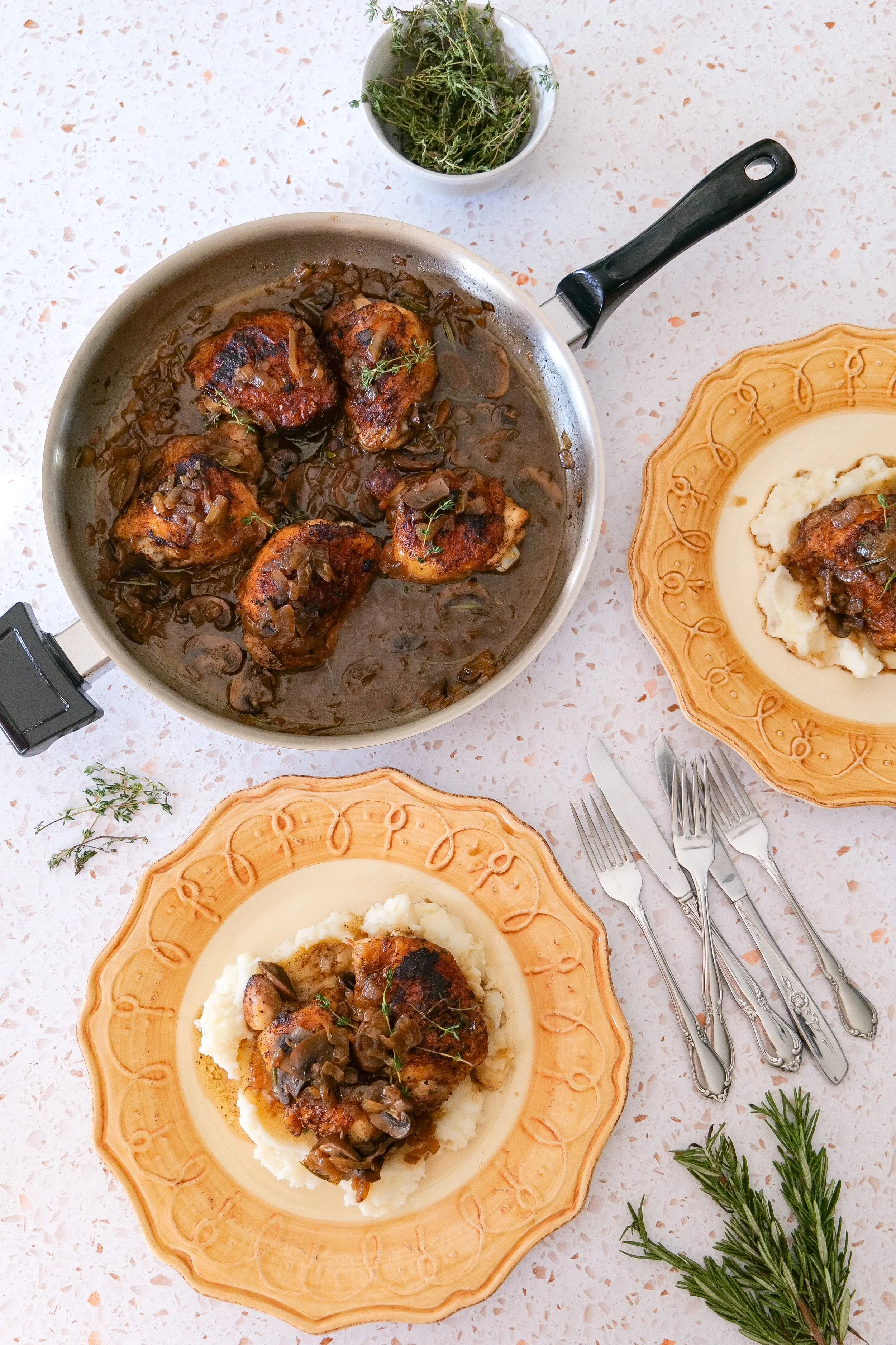 Golden chicken thighs with caramelized onions, brown mushrooms, rosemary, and thyme in a savory skillet sauce.