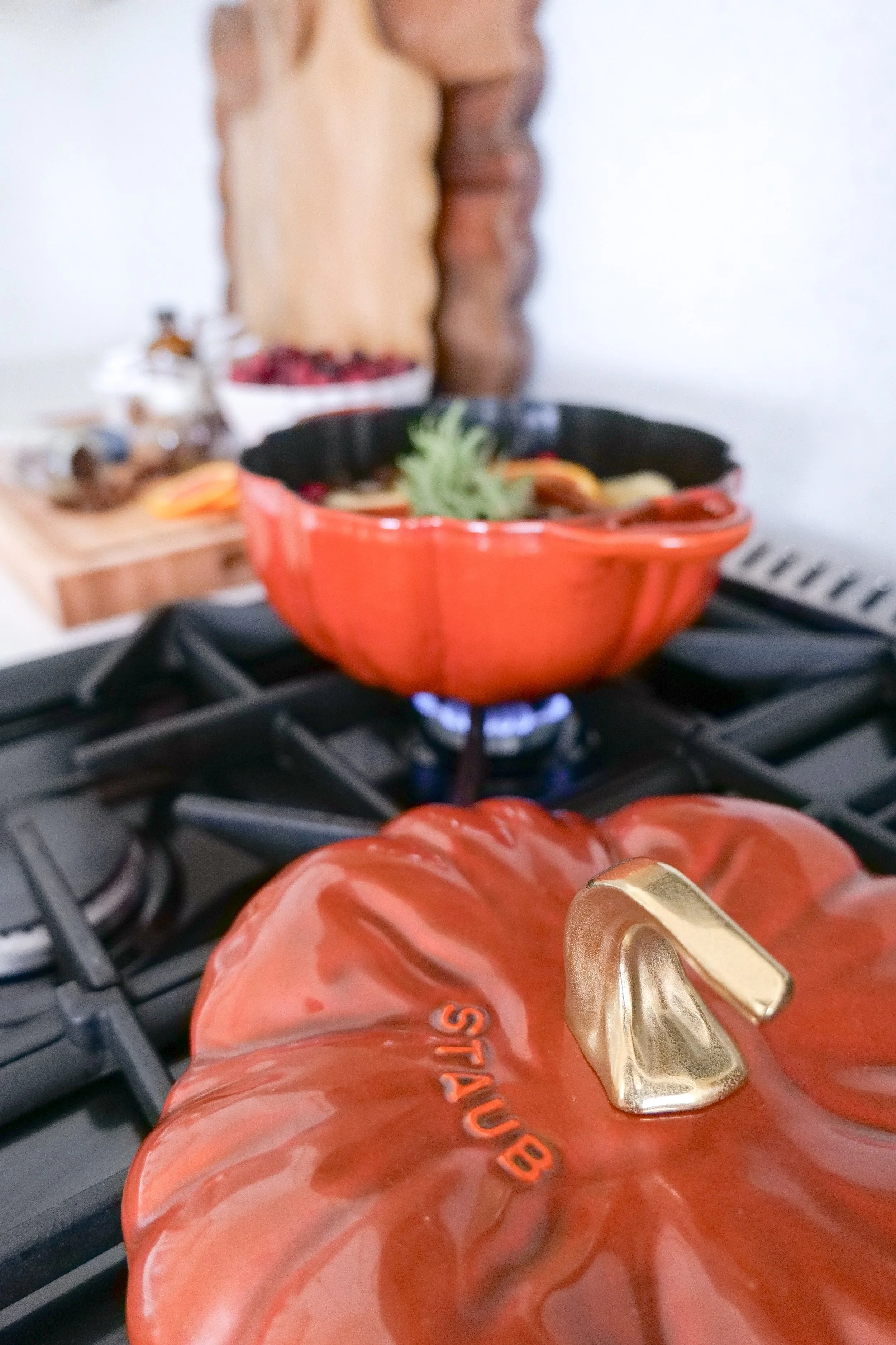 Pumpkin-shaped pot on the stovetop filled with sliced oranges, apples, cranberries, cinnamon sticks, and rosemary for a cozy fall simmer pot.