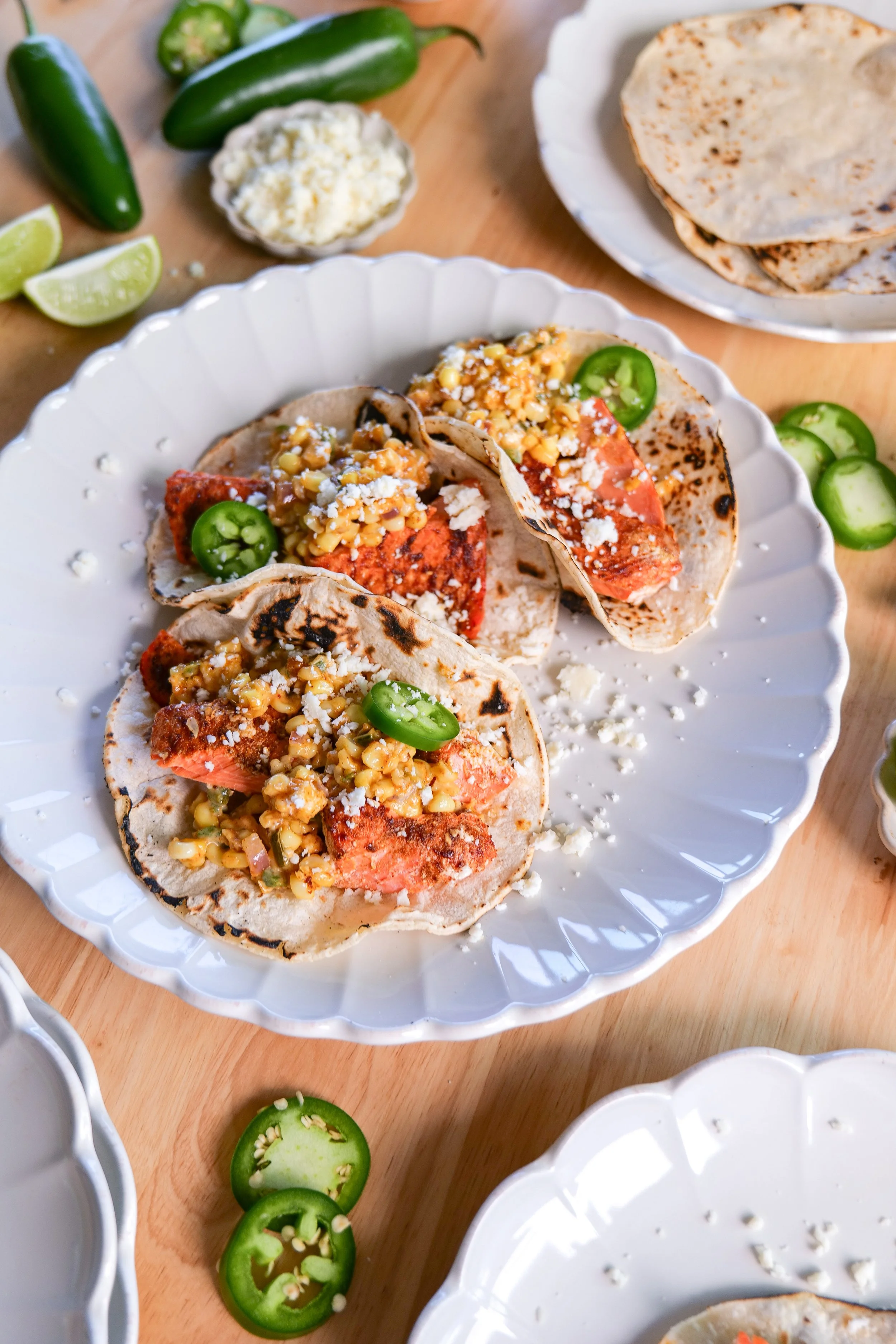 A beautifully styled table featuring homemade salmon tacos with elote corn salsa, fresh lime, and taco night accompaniments.