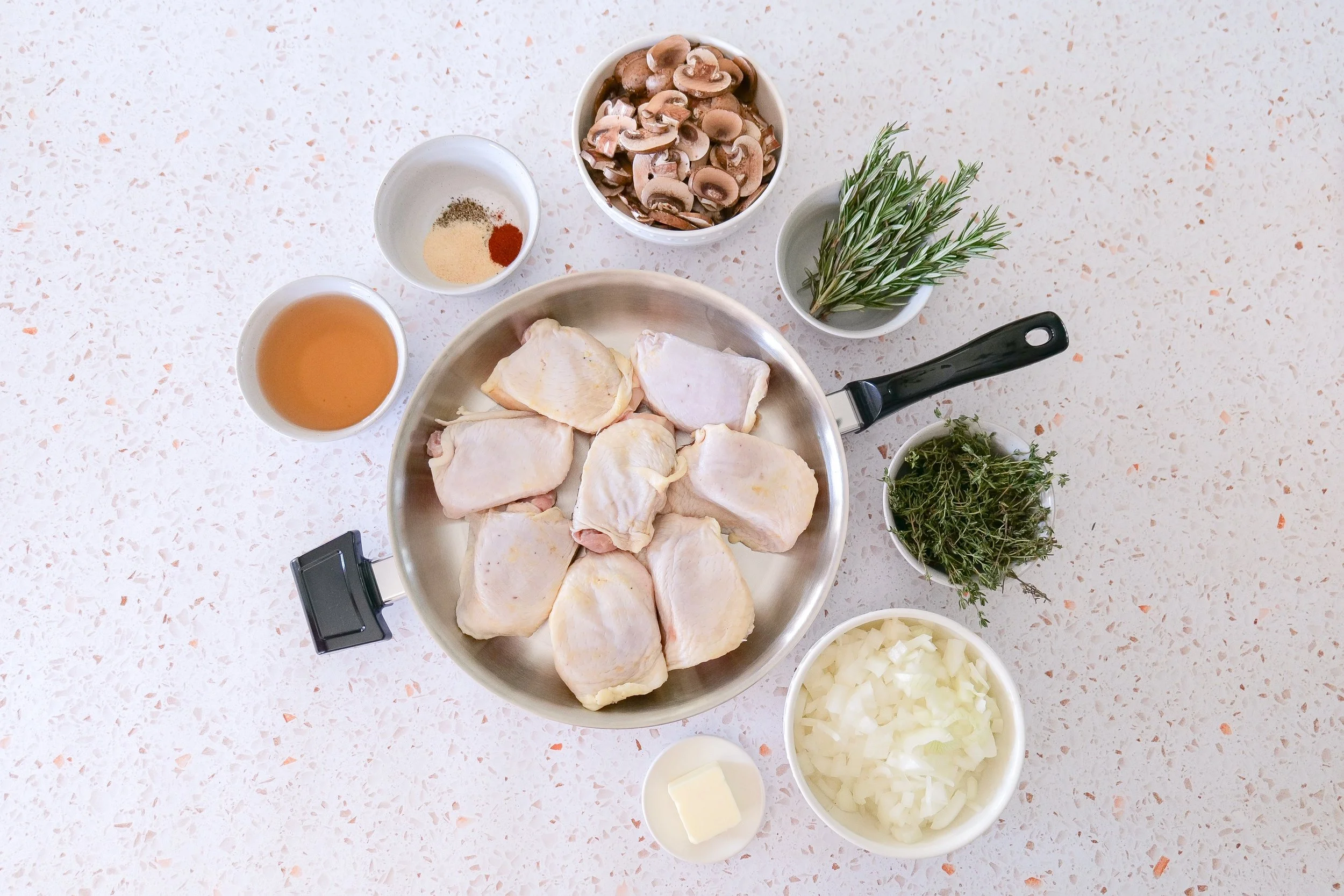 Ingredients for caramelized onion and mushroom chicken thighs with fresh herbs and seasonings.