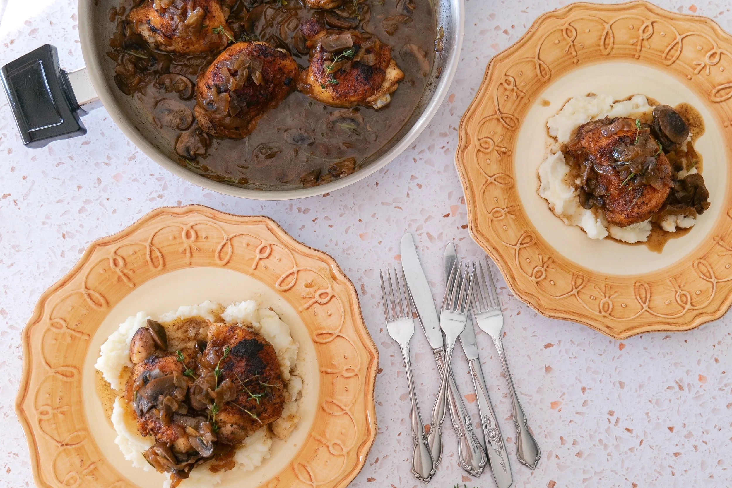Mushroom chicken thighs in a skillet with caramelized onions and fresh herbs.