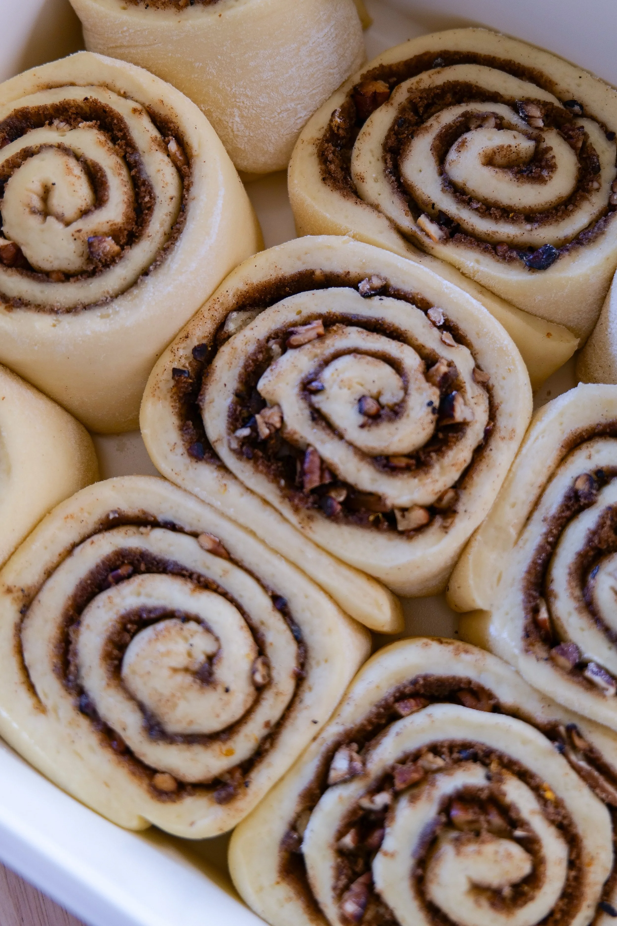 Unbaked orange pecan cinnamon rolls arranged in a baking dish before rising and baking.