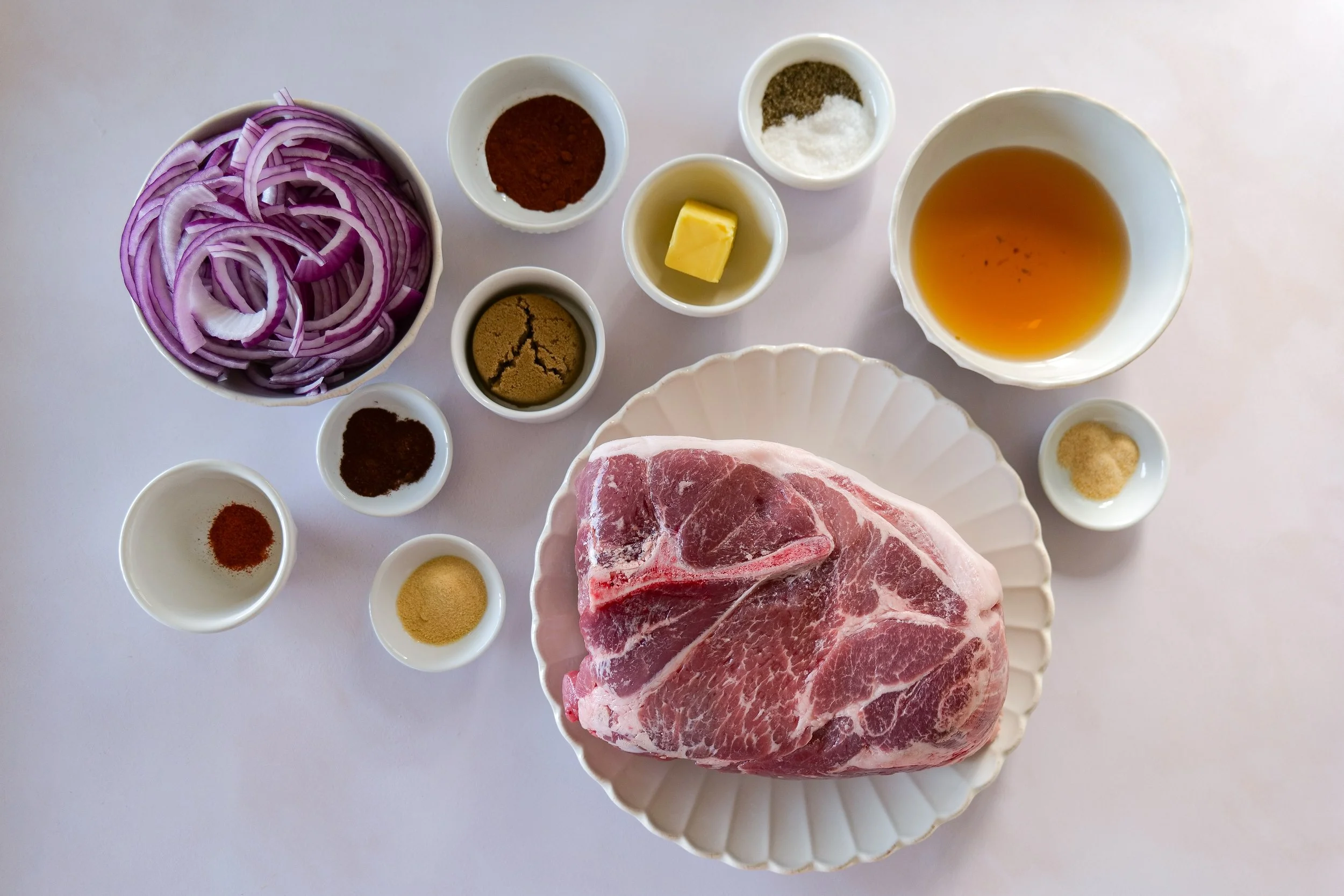 Ingredients for easy slow cooker pulled pork including pork shoulder, red onion, chicken broth, olive oil and dry rub seasonings.