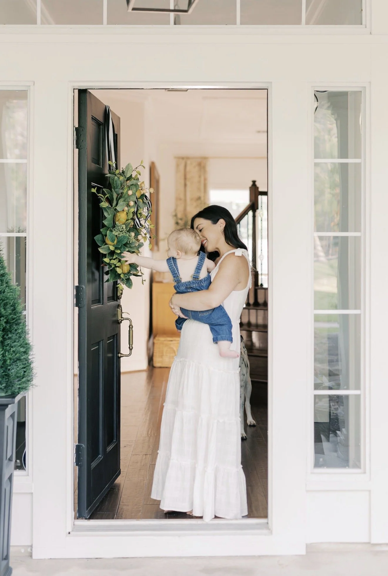 Mom smiling as her baby reaches for the wreath on the front door of their Texas home