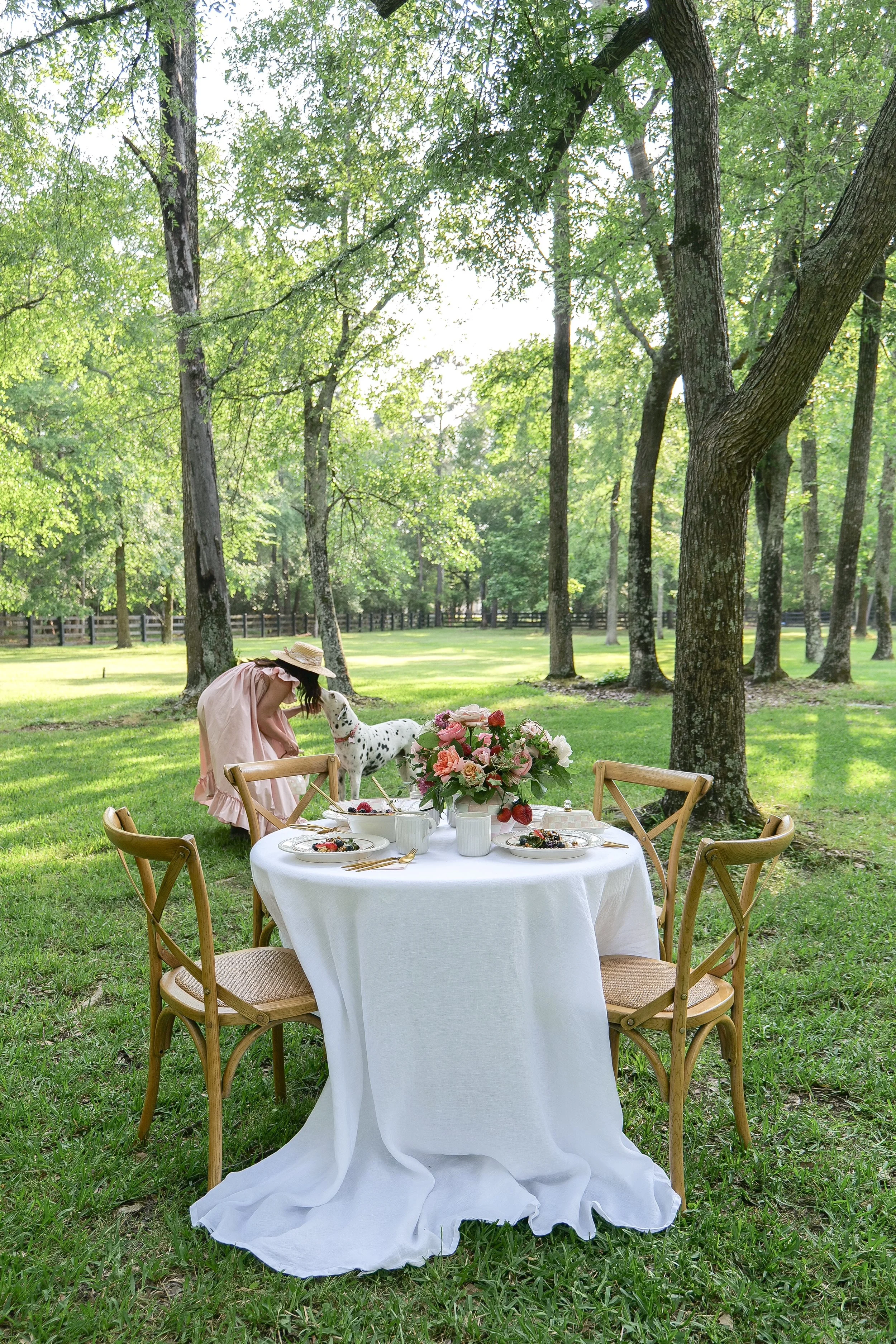 Elegant outdoor garden lunch table setting surrounded by trees and summer greenery.
