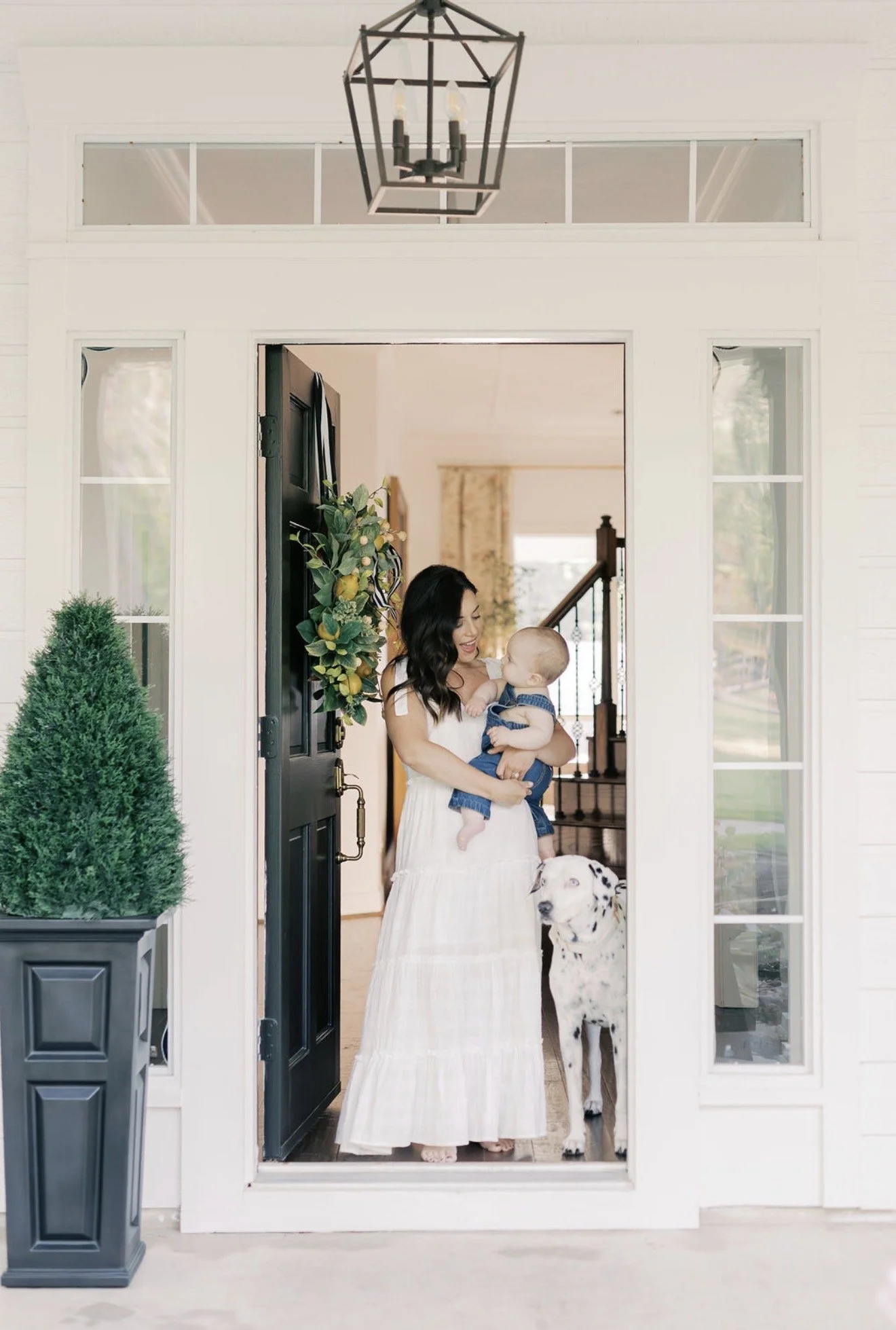 Mom holding her baby beside their Dalmatian at the open front door of their Texas home