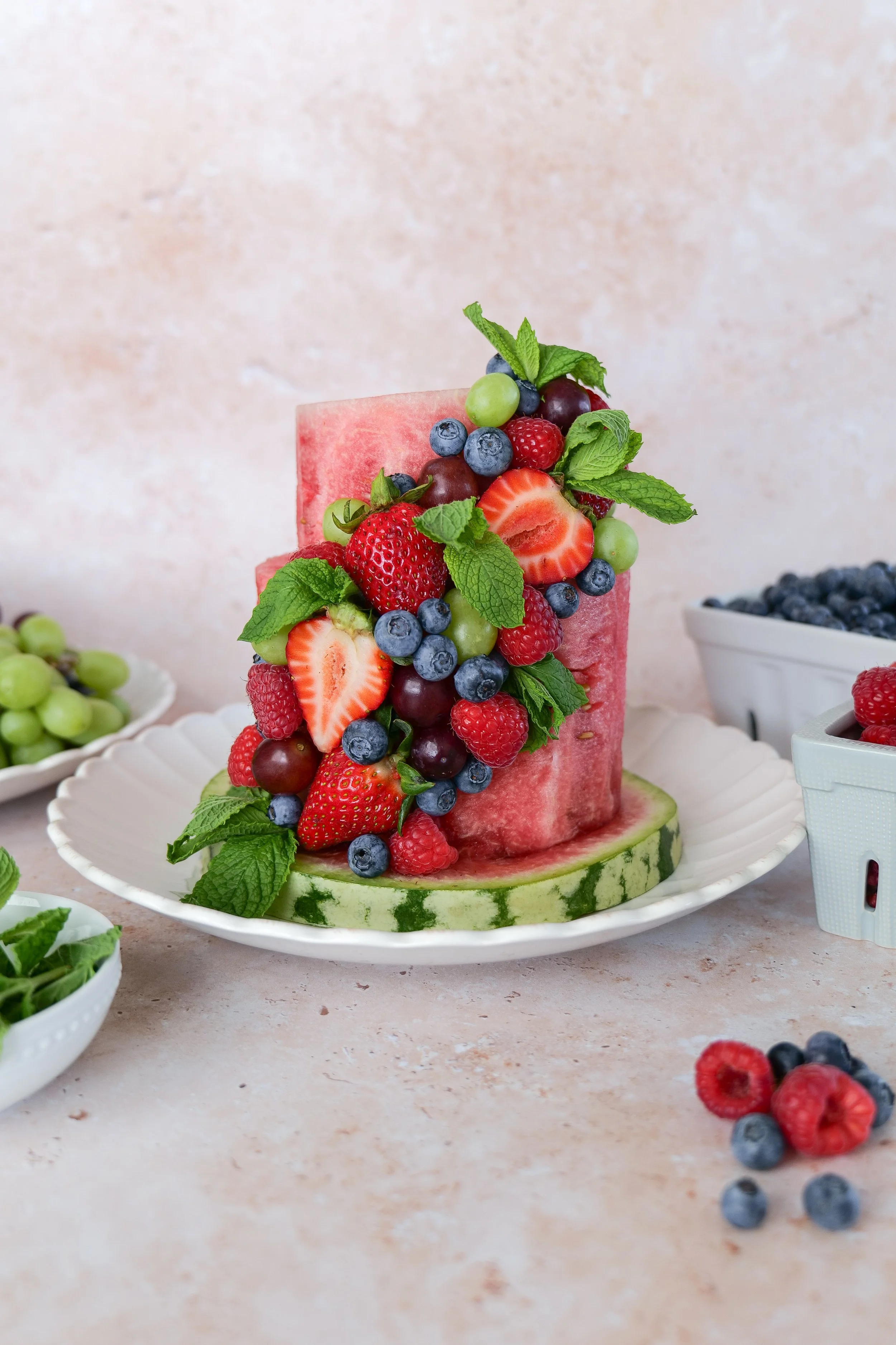 Watermelon fruit cake decorated with raspberries, blueberries, strawberries, and grapes in several colors.