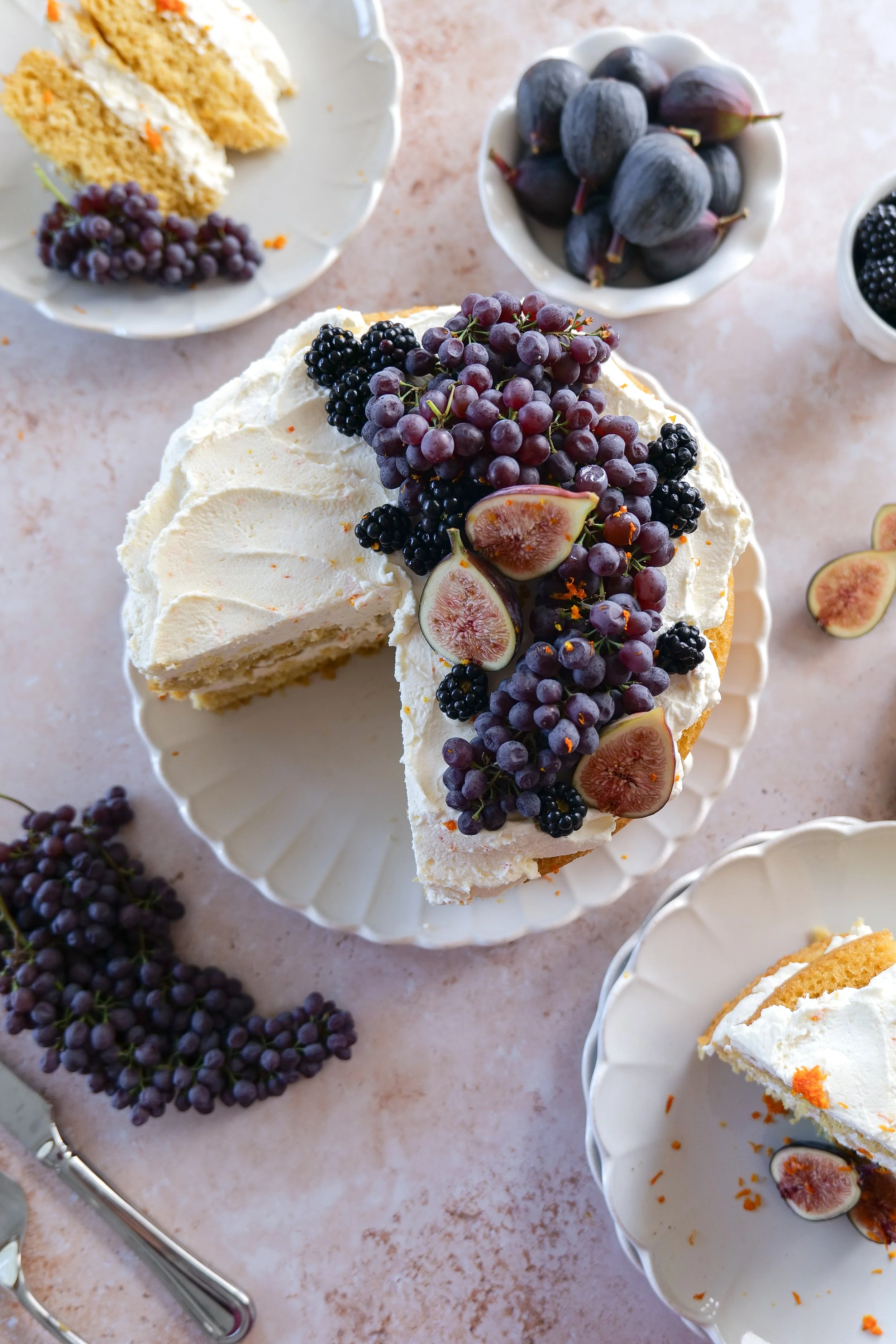 Overhead view of sliced orange olive oil cake with fresh fruit arranged in bowls around the cake