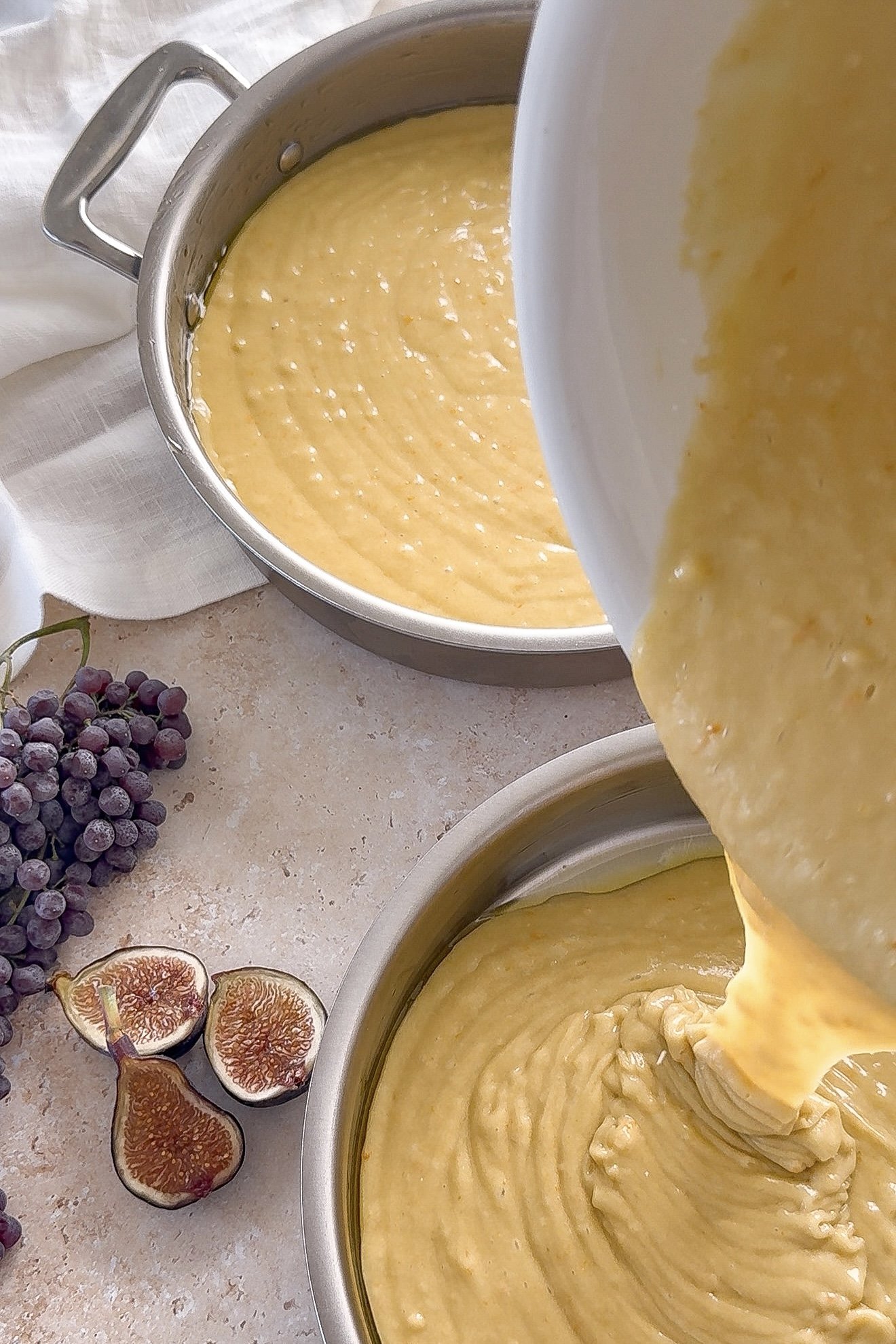 Orange olive oil cake batter being divided between two round cake pans