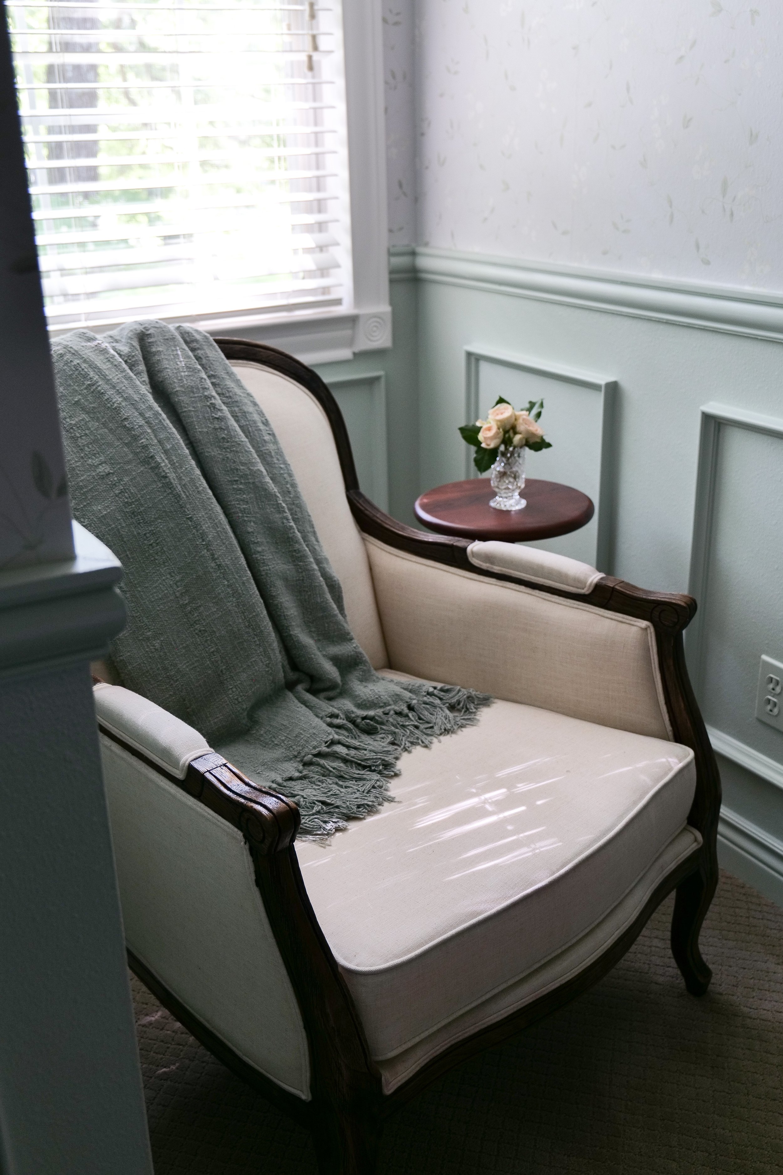 Cozy reading chair in traditional guest bedroom styled with soft throw blanket and pillows.
