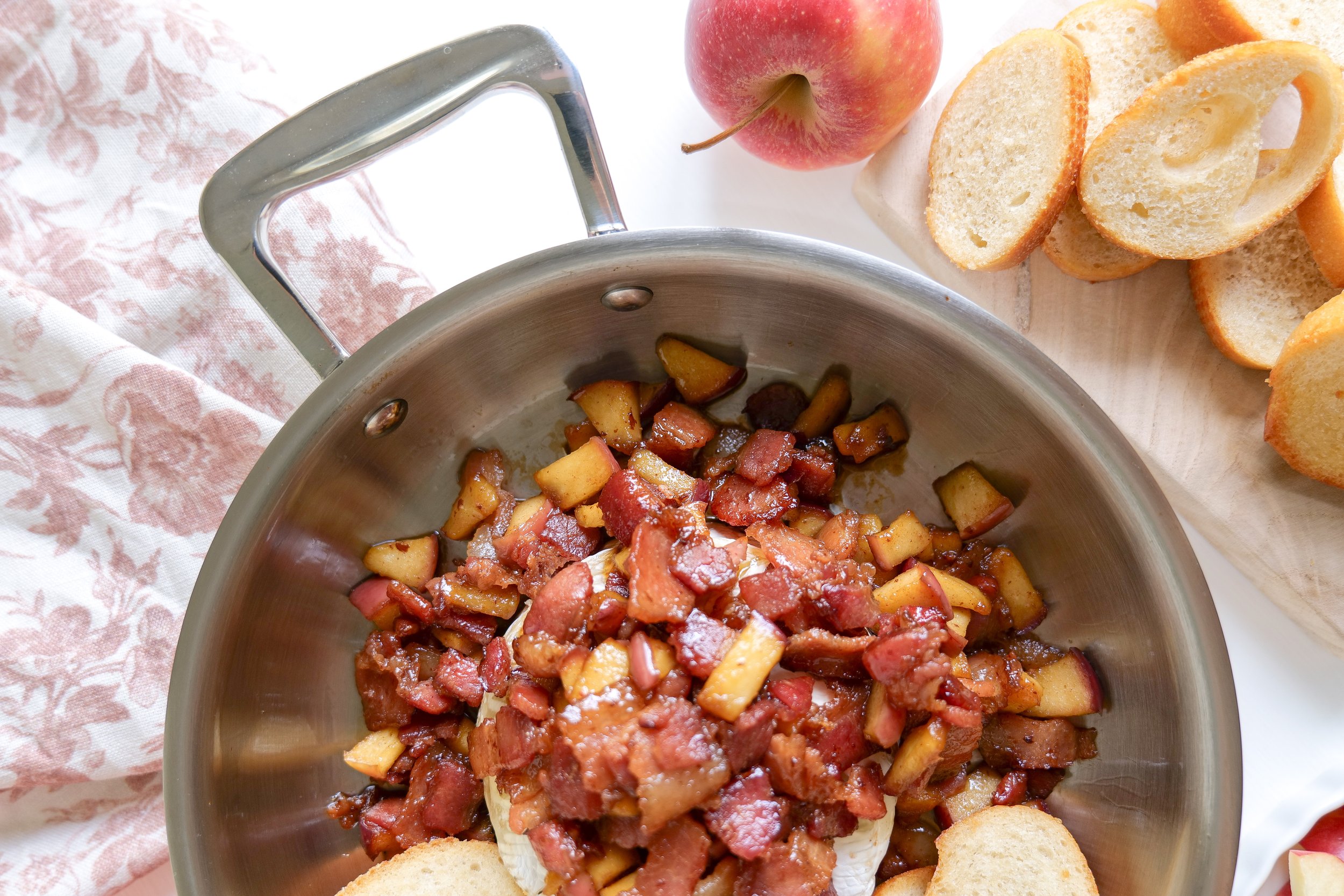 Close-up of creamy baked brie topped with crispy bacon and tender apples.
