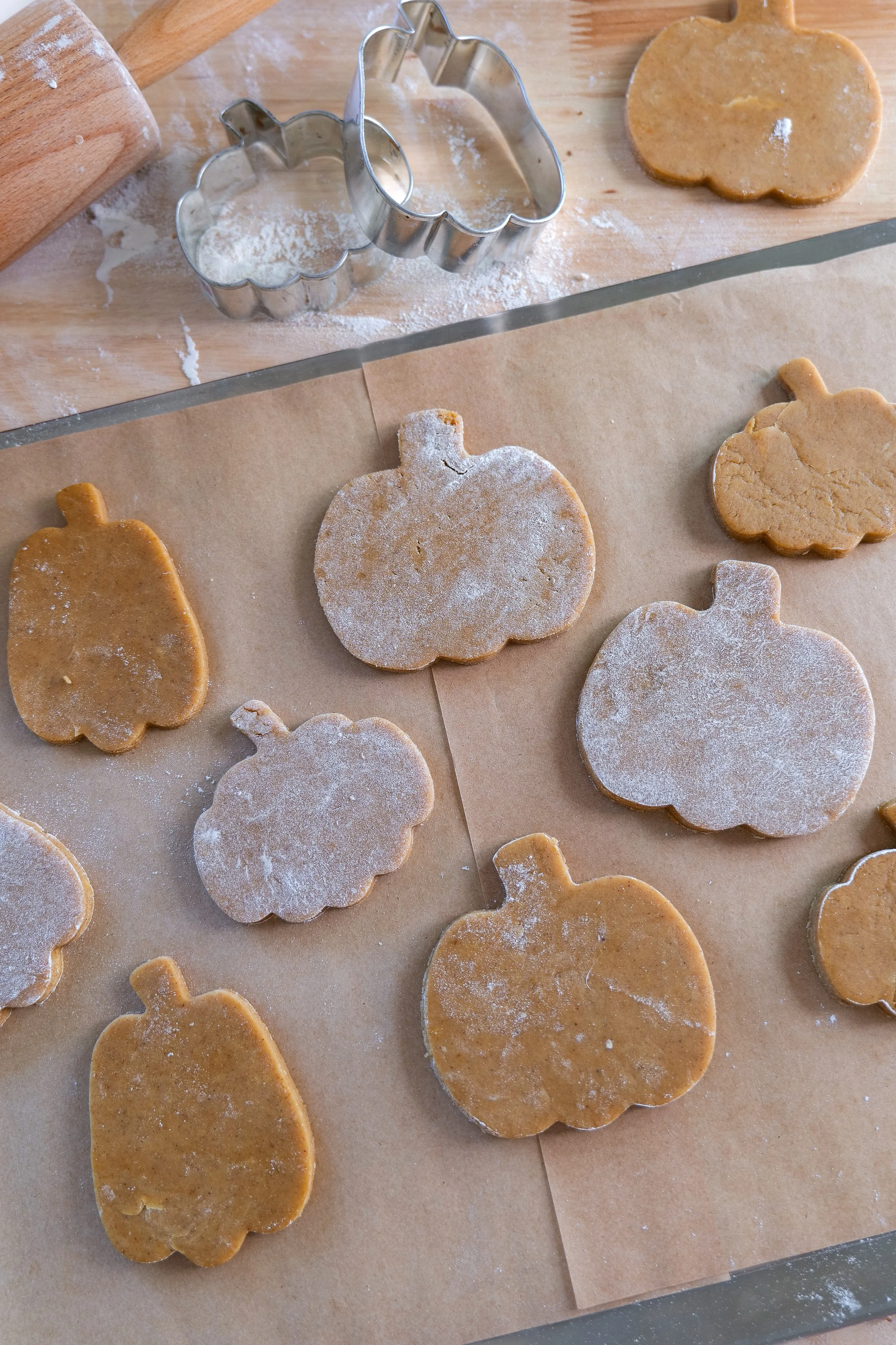 Pumpkin cutout cookies arranged on a parchment-lined baking sheet before baking