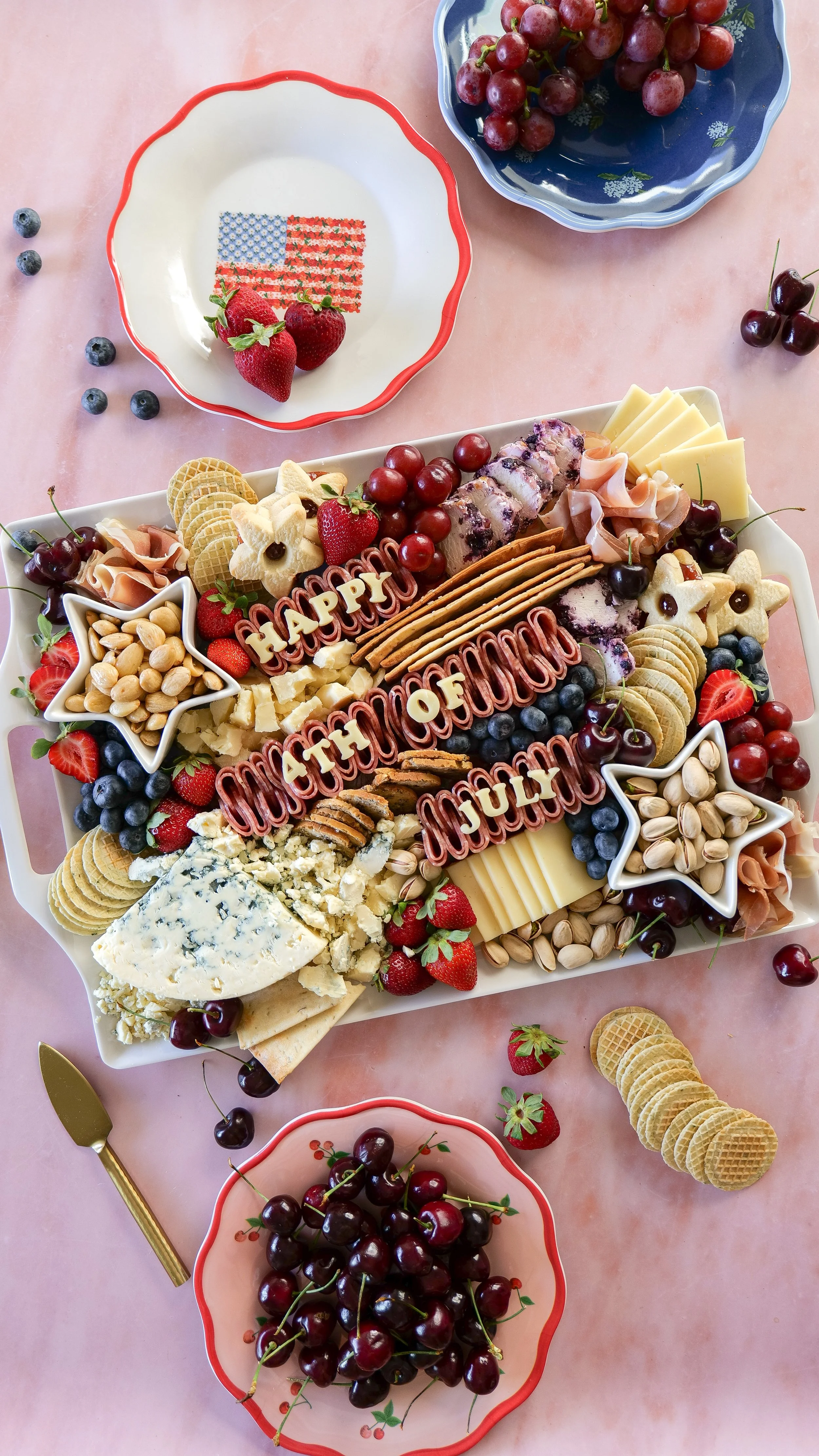 Charcuterie board spelling out Happy Fourth of July with festive red, white, and blue ingredients.