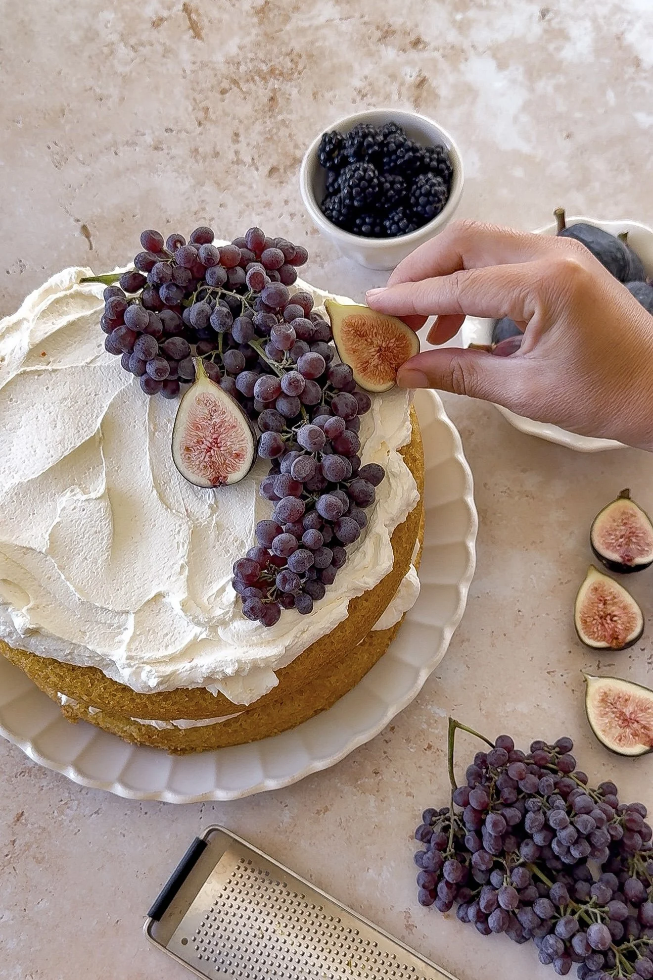 Decorating orange olive oil cake with fresh figs, blackberries, and champagne grapes