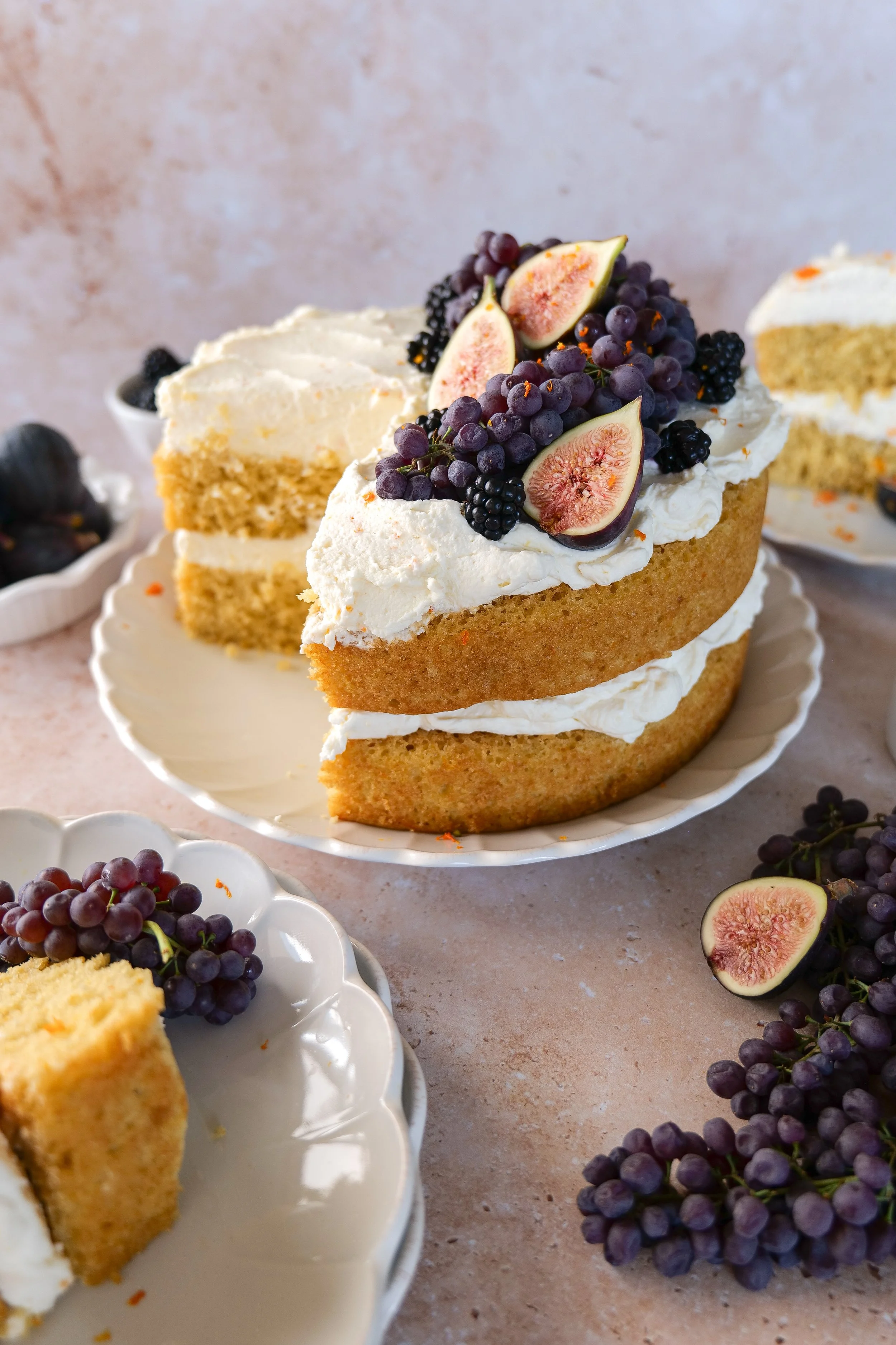 Slices of orange olive oil cake with mascarpone cream arranged in front of the remaining fresh fruit cake