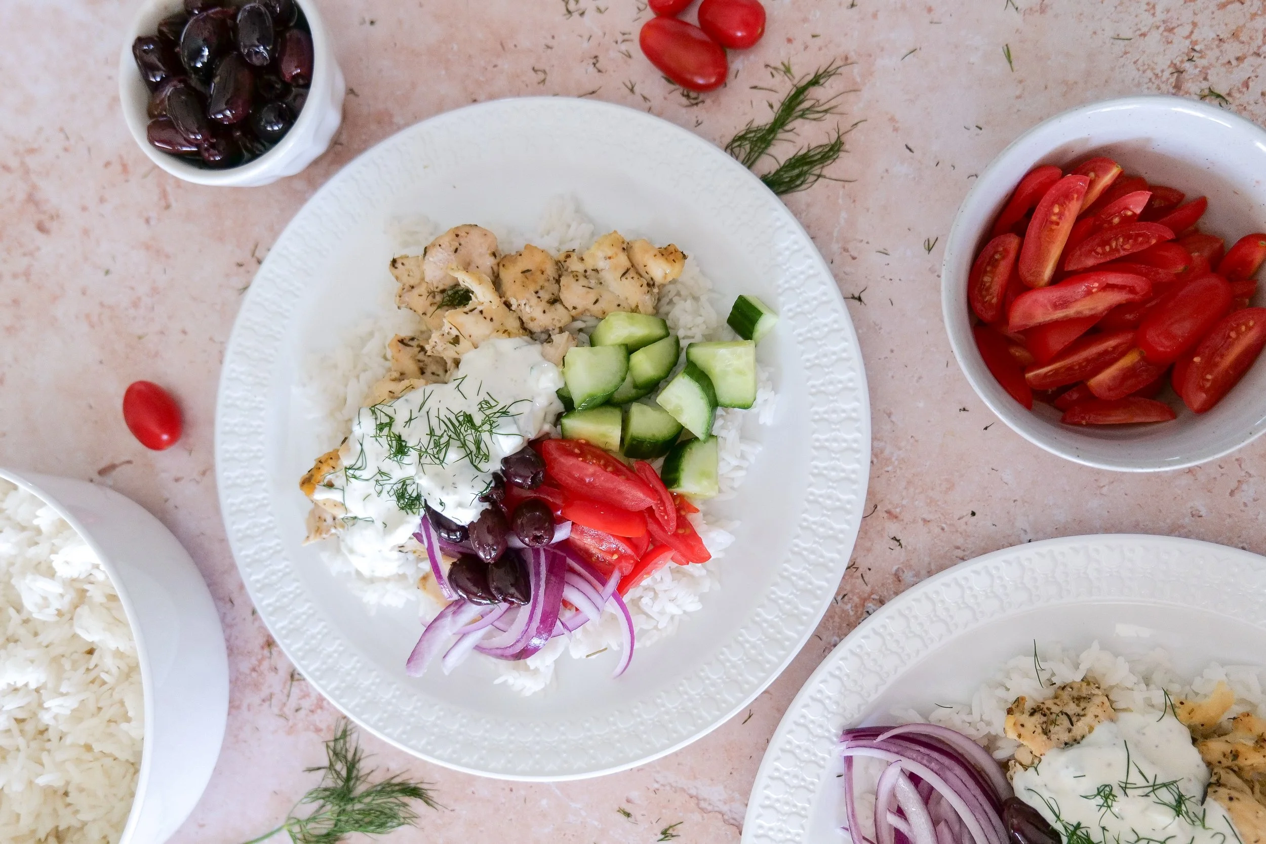 Close-up of herb chicken and jasmine rice topped with cucumber, tomatoes, olives and creamy tzatziki.