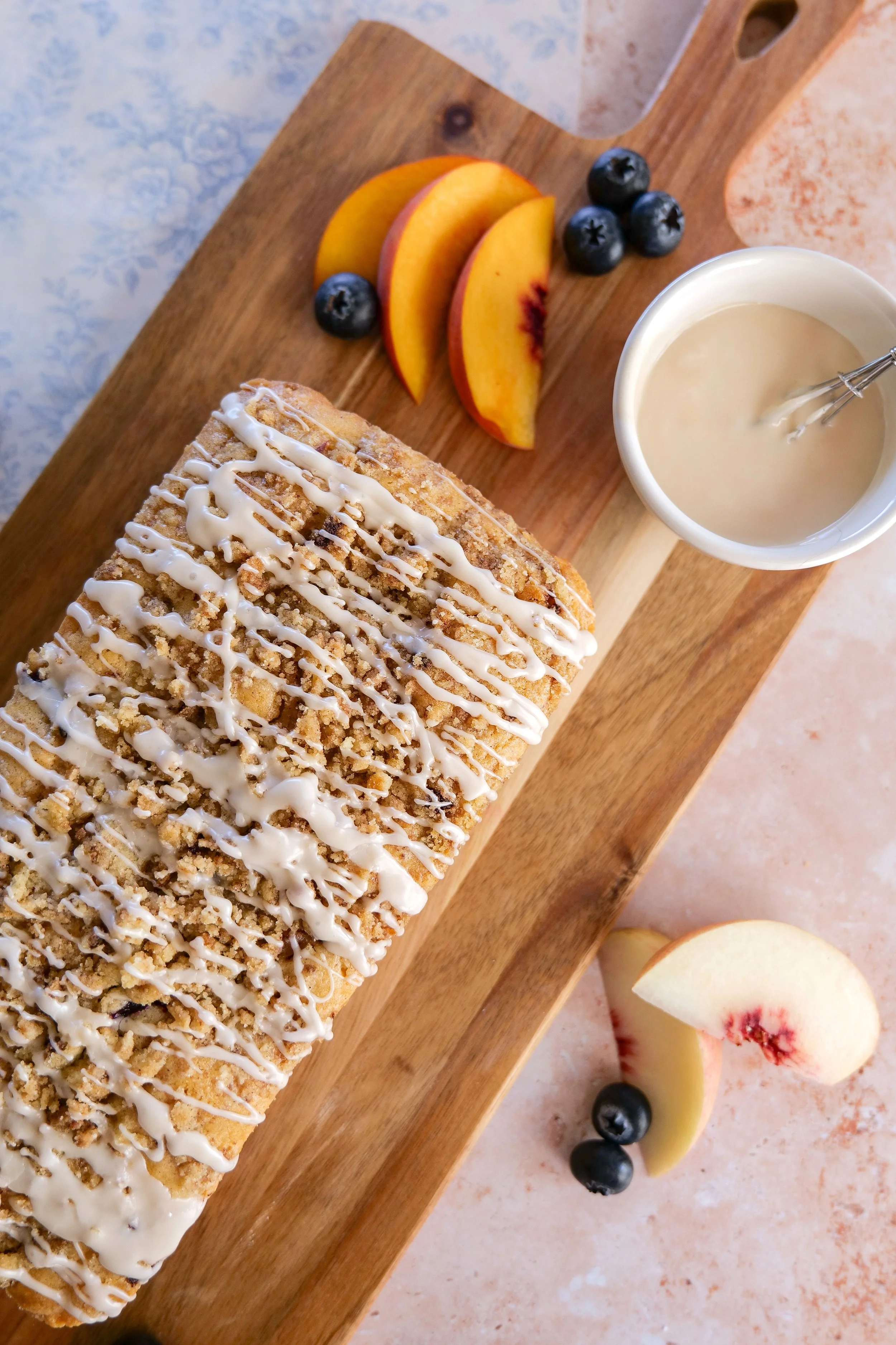 Slice of Blueberry Peach Bread topped with cinnamon streusel and a drizzle of vanilla glaze.