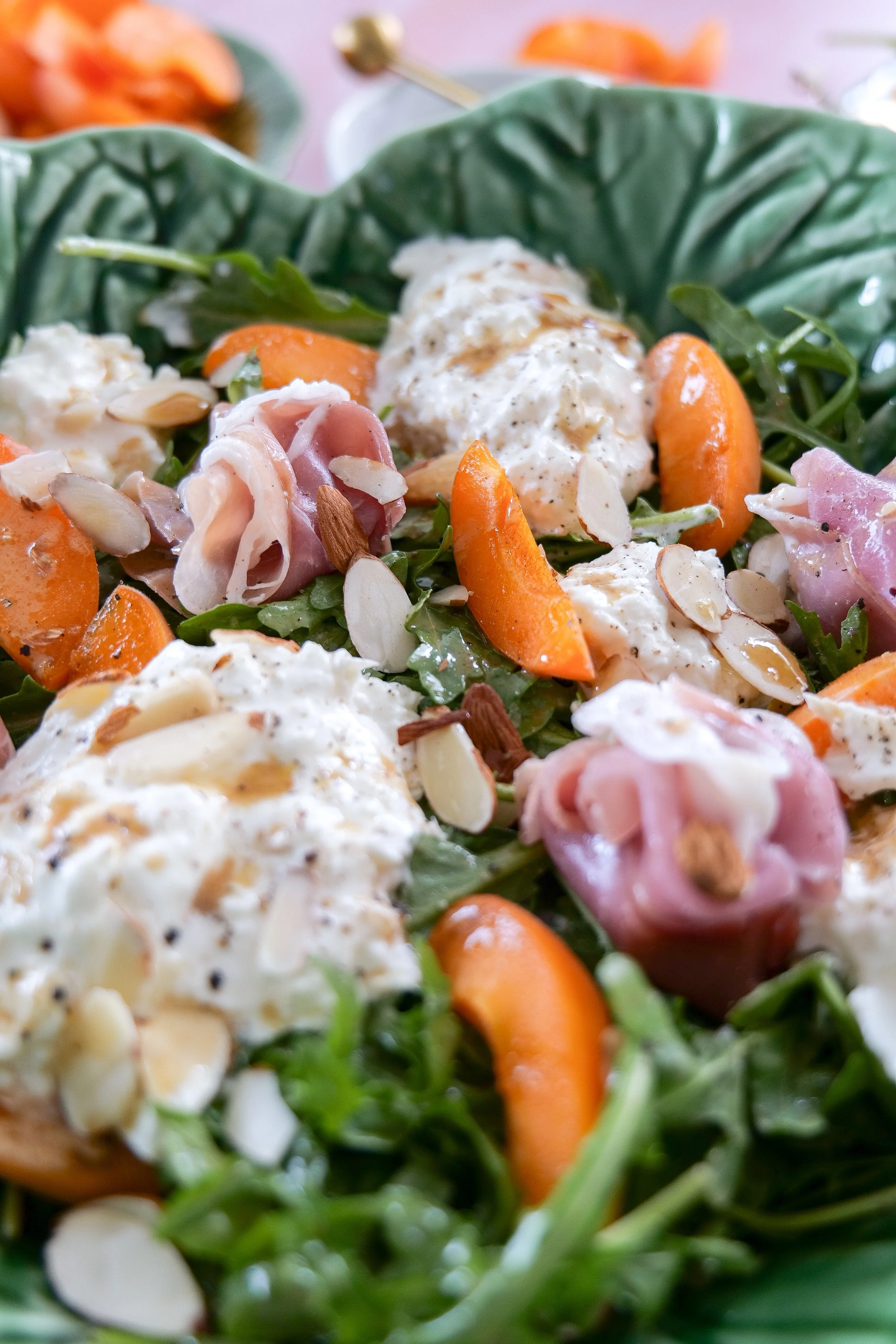 Stone fruit burrata salad with arugula and prosciutto slices.
