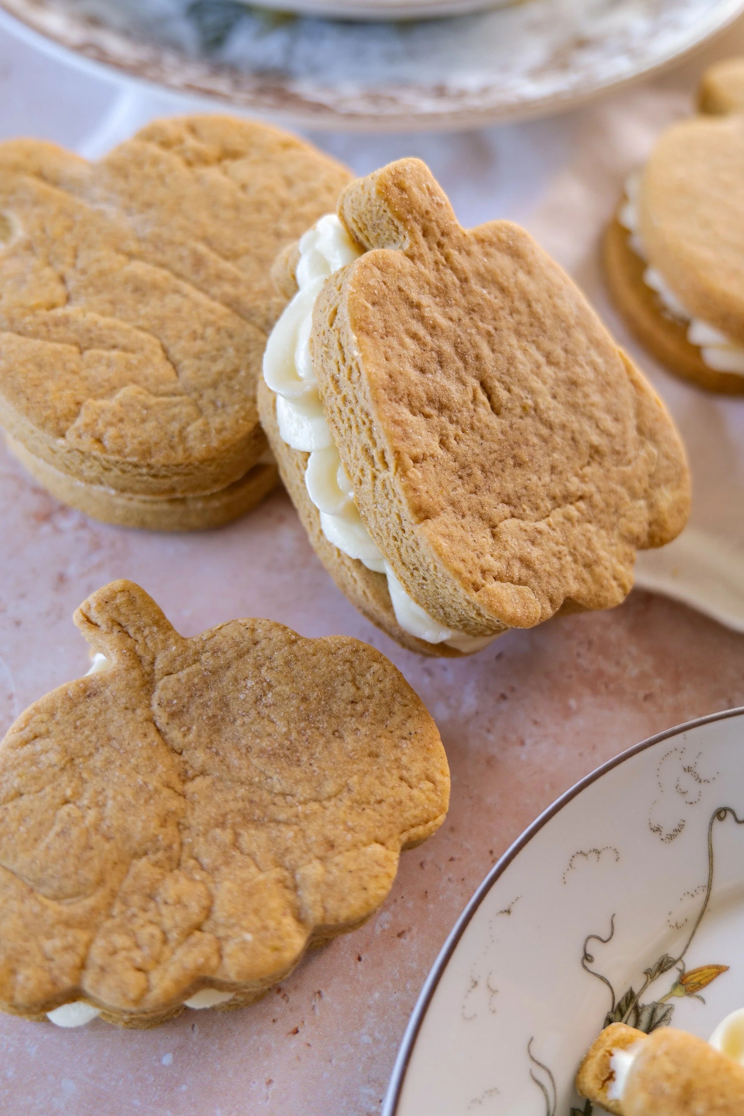 Pumpkin sandwich cookie with a thick vanilla cream cheese center between two soft brown butter pumpkin cookies