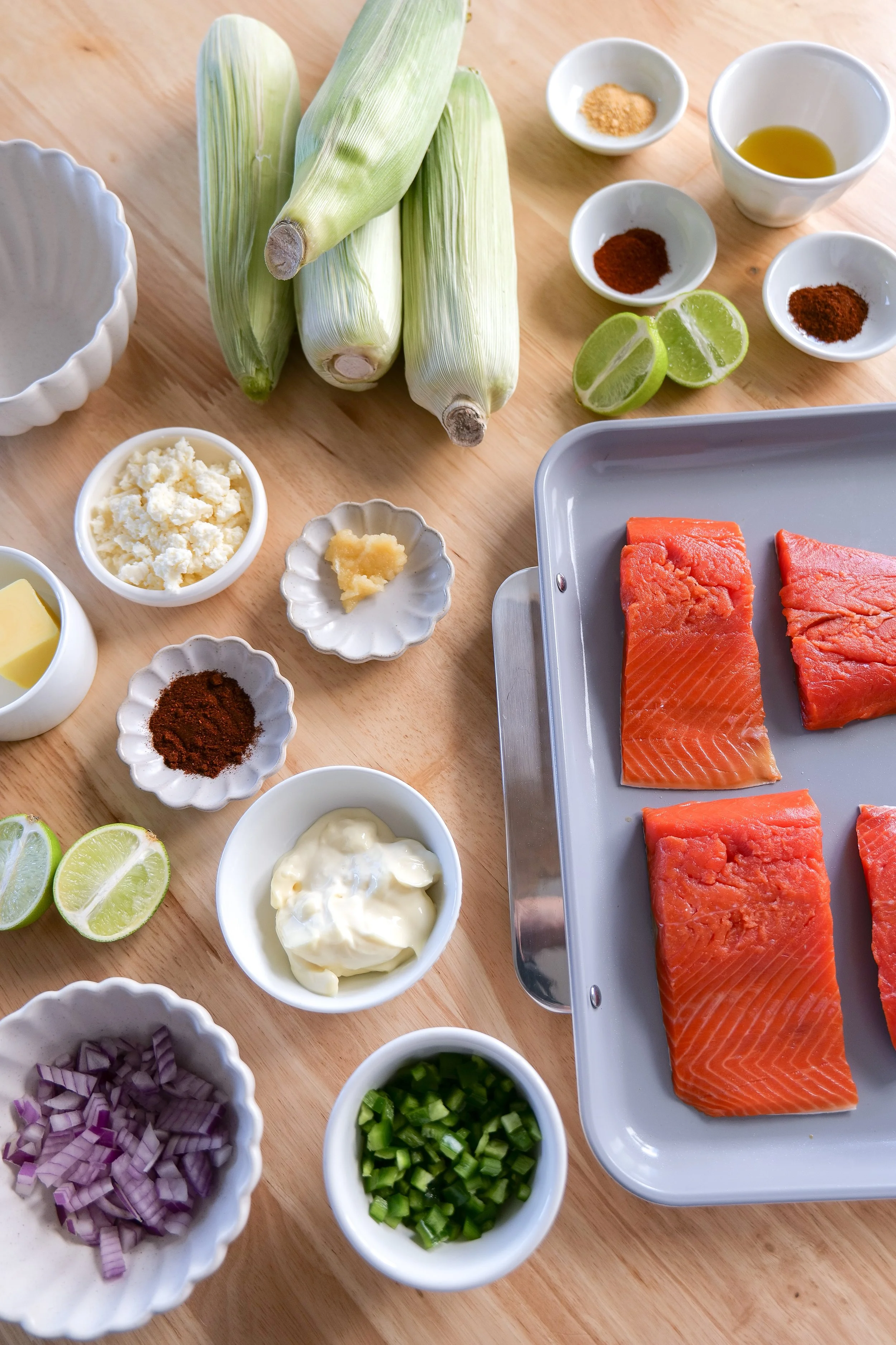 Ingredients for salmon tacos including salmon, fresh corn, lime, cotija cheese, and seasonings