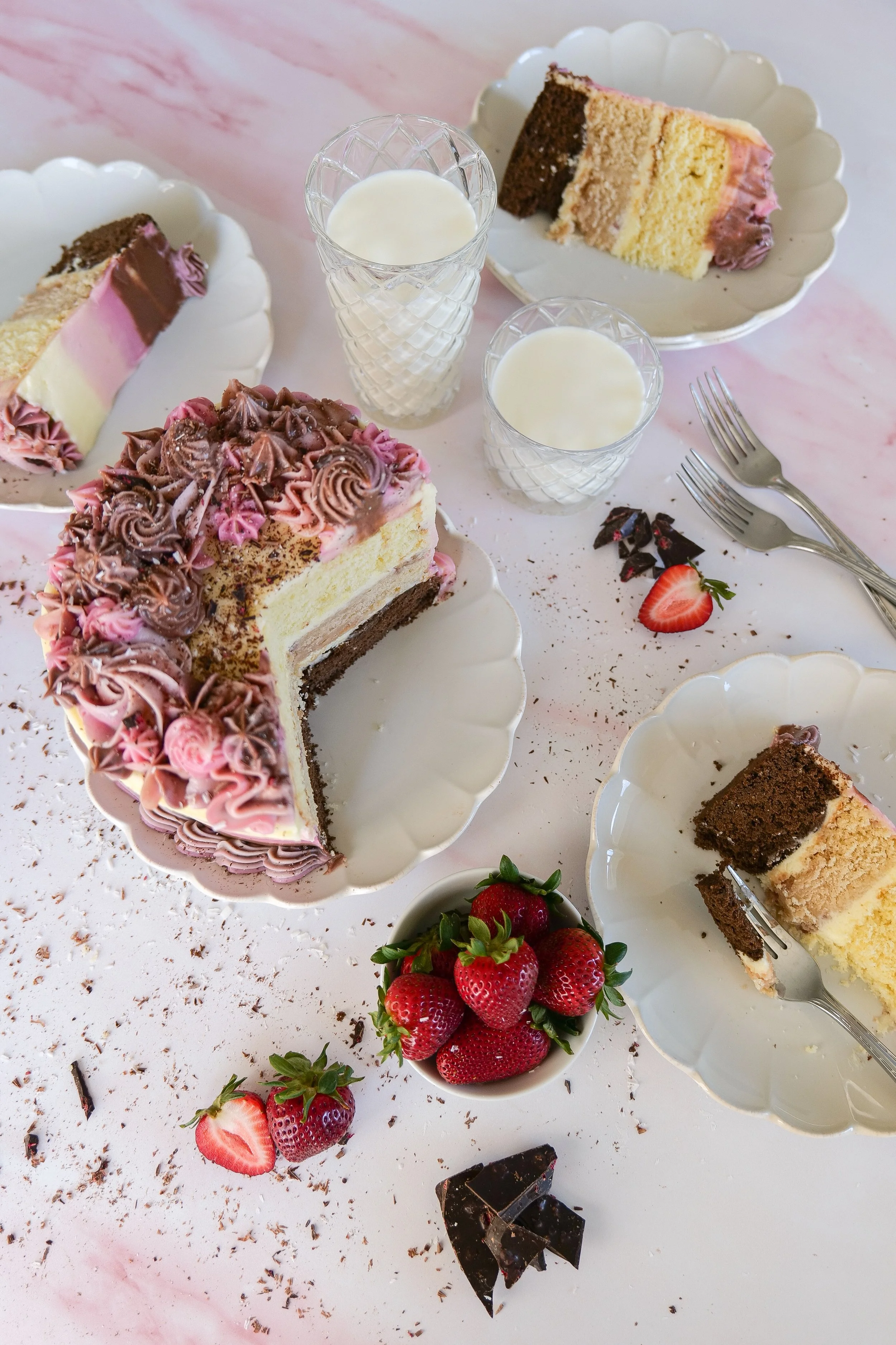 Neapolitan cake served with fresh strawberries and glasses of milk on a table.