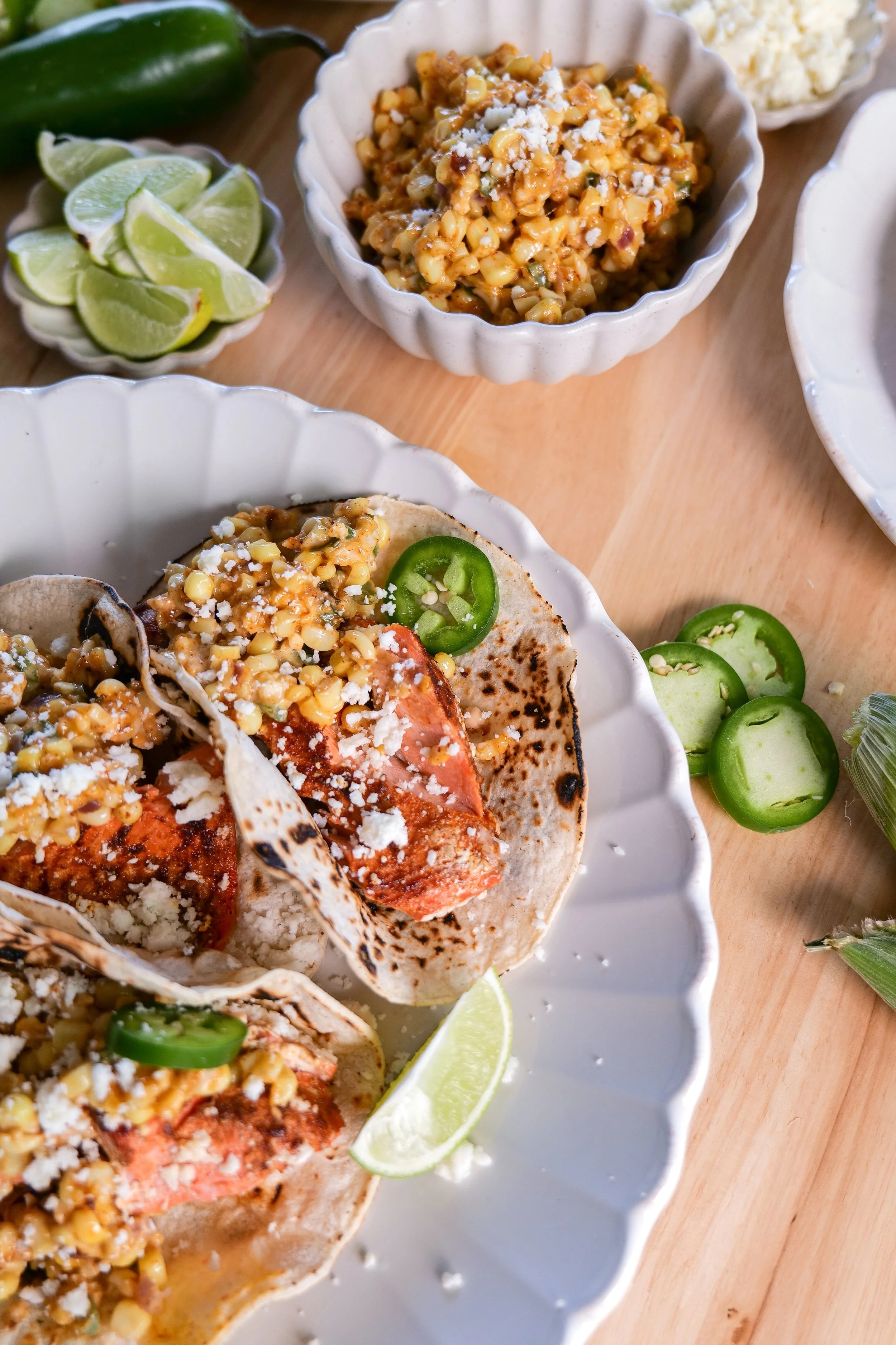 Detailed view of baked salmon tacos topped with elote corn salsa, crumbled cotija cheese, and fresh lime.