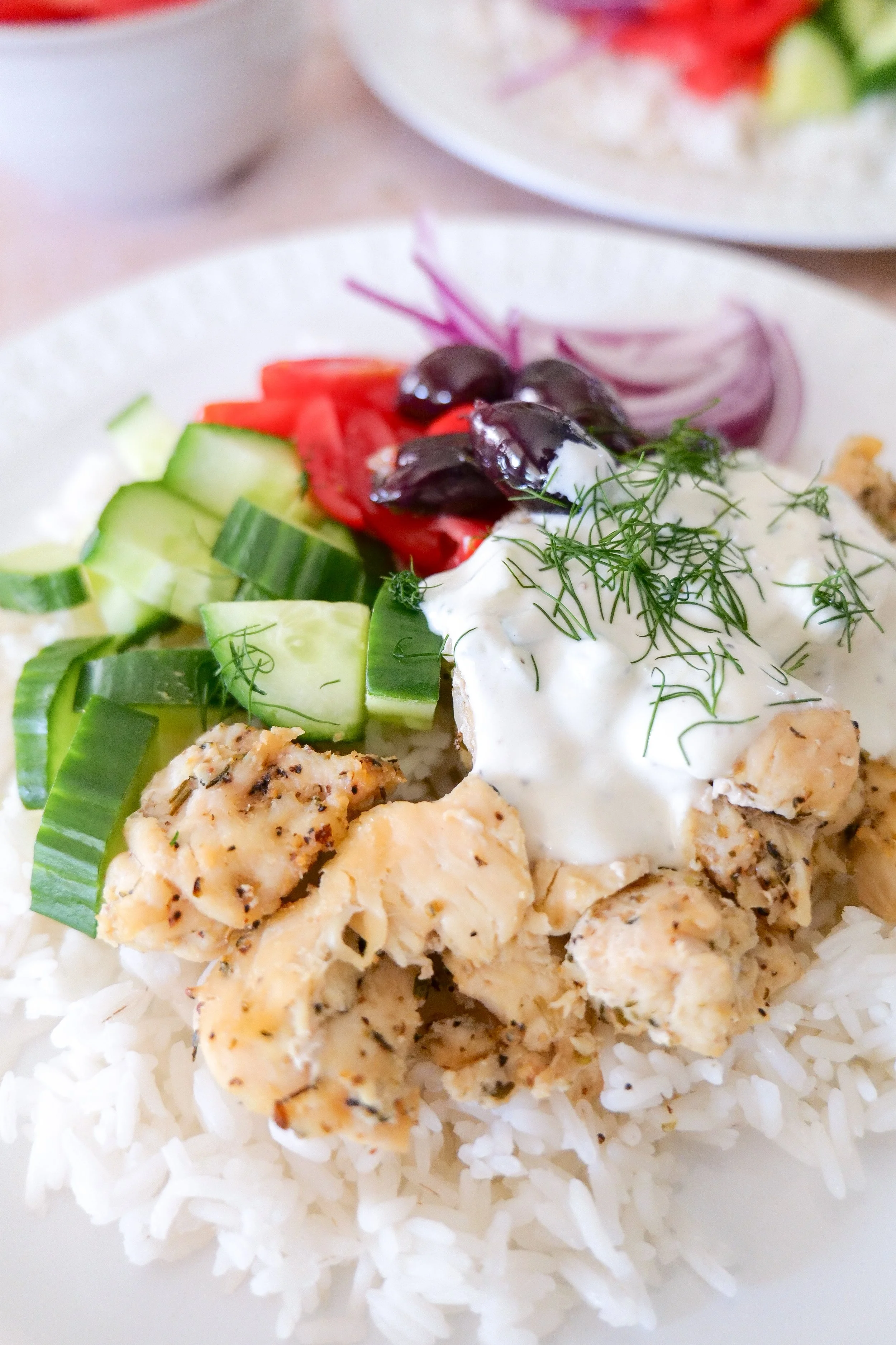 Overhead view of Greek-inspired chicken and jasmine rice bowl with fresh vegetables and tzatziki.