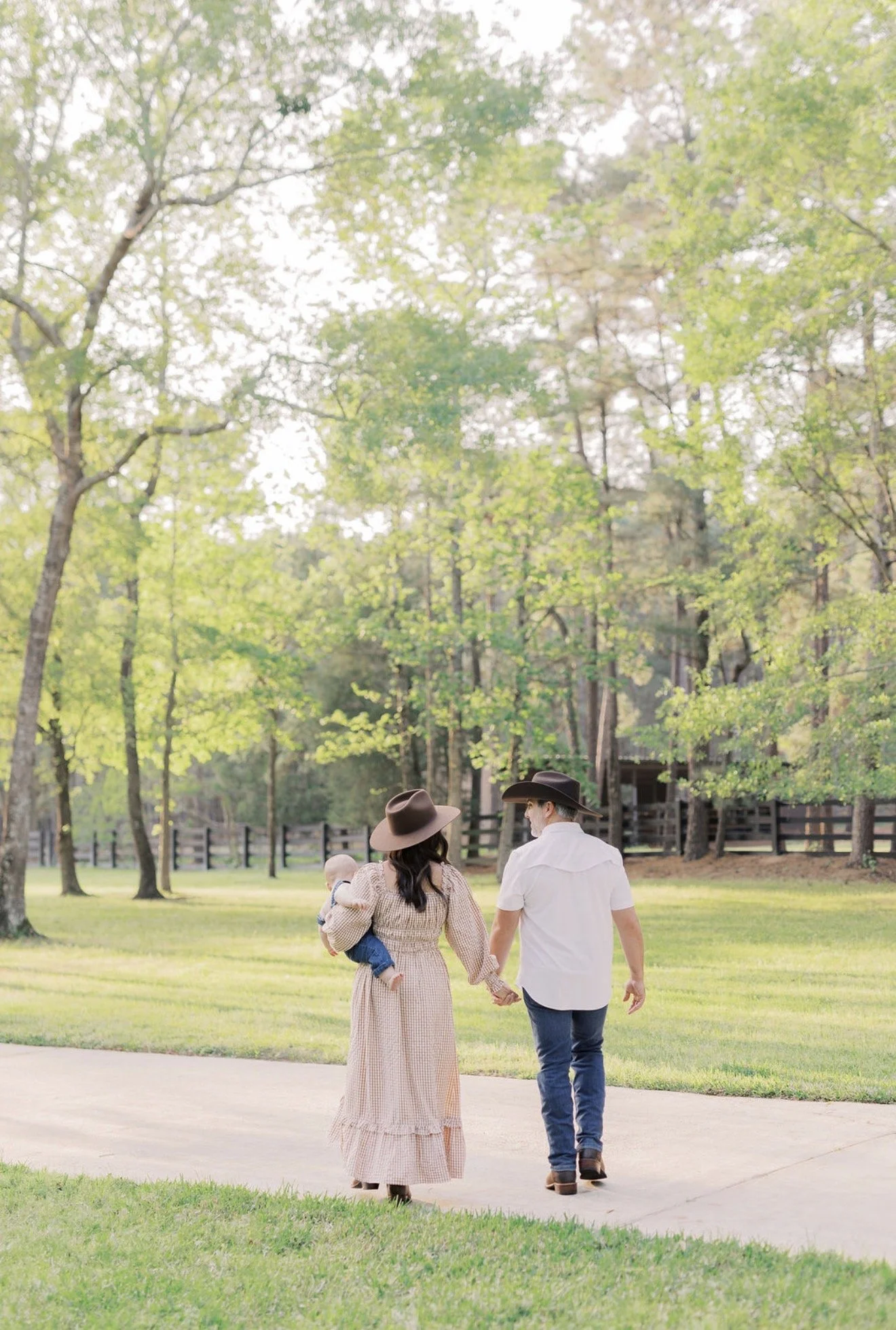 Mom and dad wearing cowboy hats and walking hand in hand with their baby on their Texas property