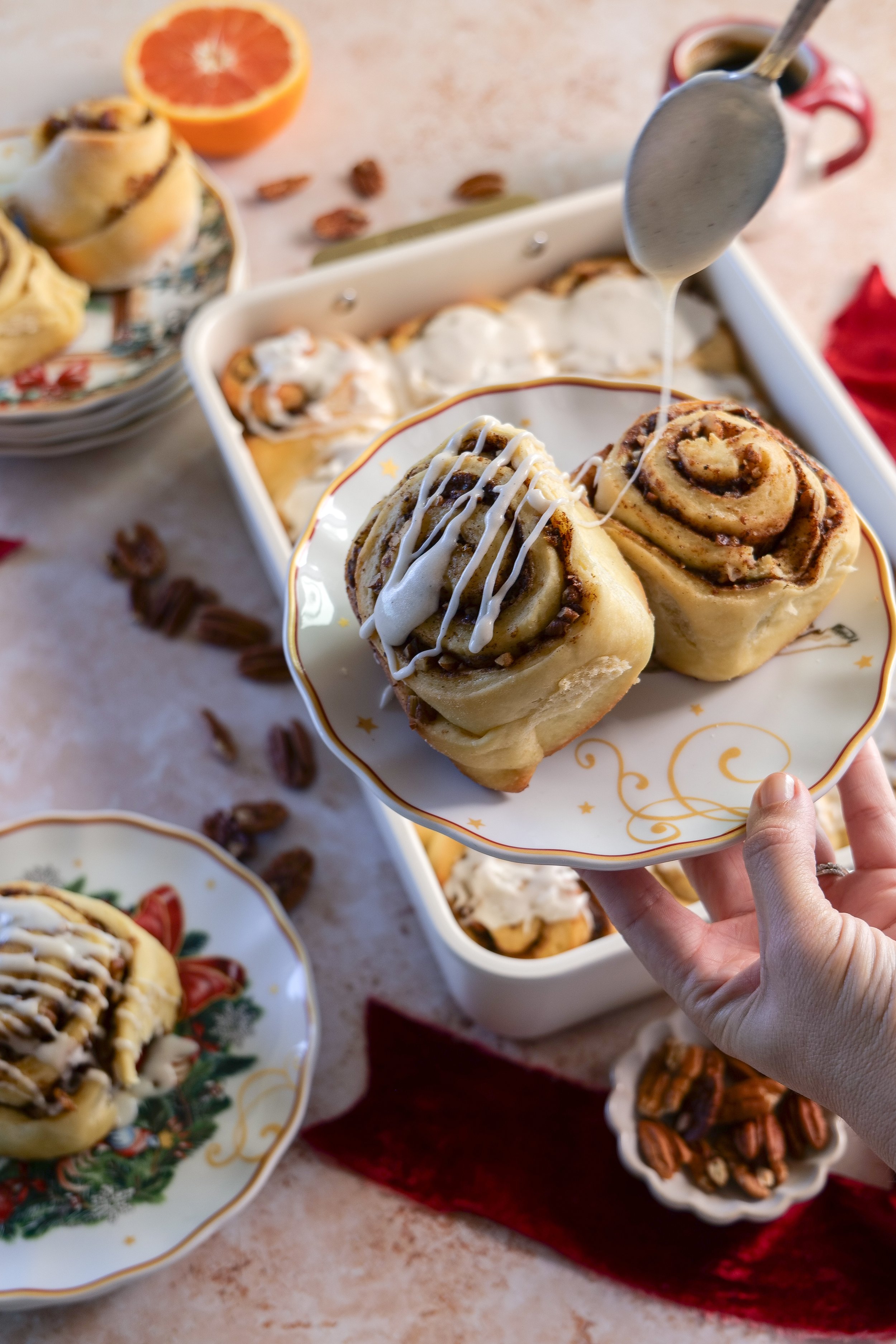 Vanilla bean glaze being drizzled over warm brown butter orange pecan cinnamon rolls.