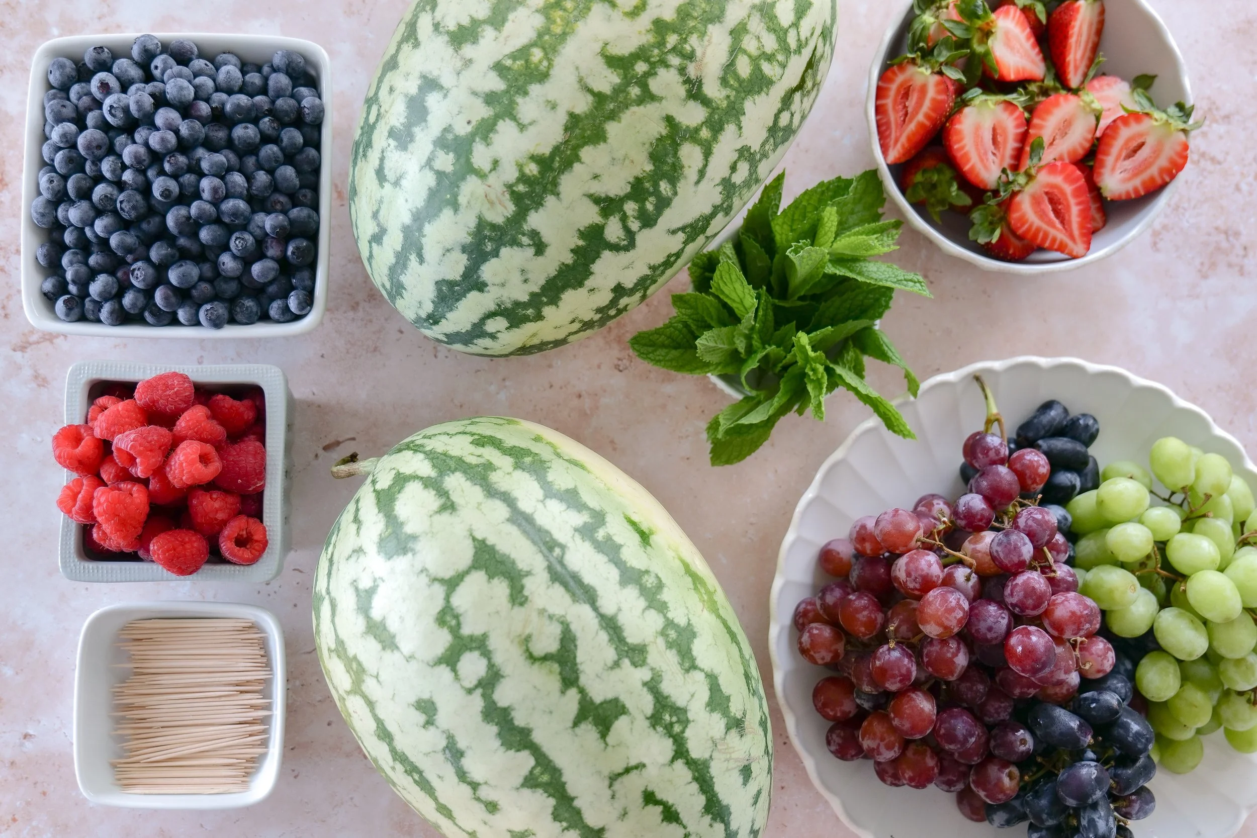 Fresh strawberries, raspberries, blueberries, and colorful grapes prepared for decorating a watermelon fruit cake.