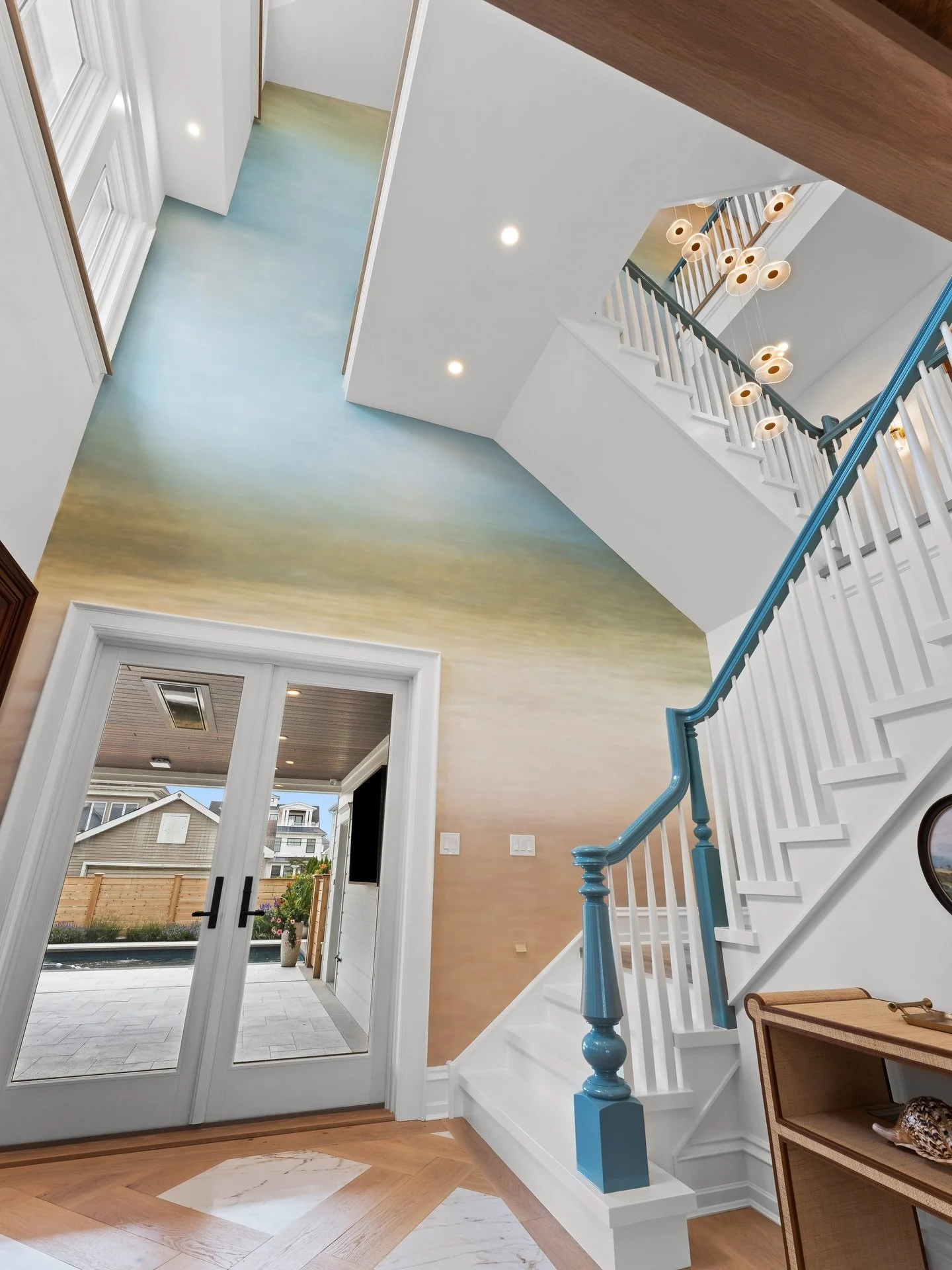 A coastal stairwell that feels like pure magic ✨The custom-painted accent wall sets the tone, while a sculptural chandelier draws your eye upward, turning a simple pass-through into a true statement moment. The blue high-gloss railing adds a bold, po