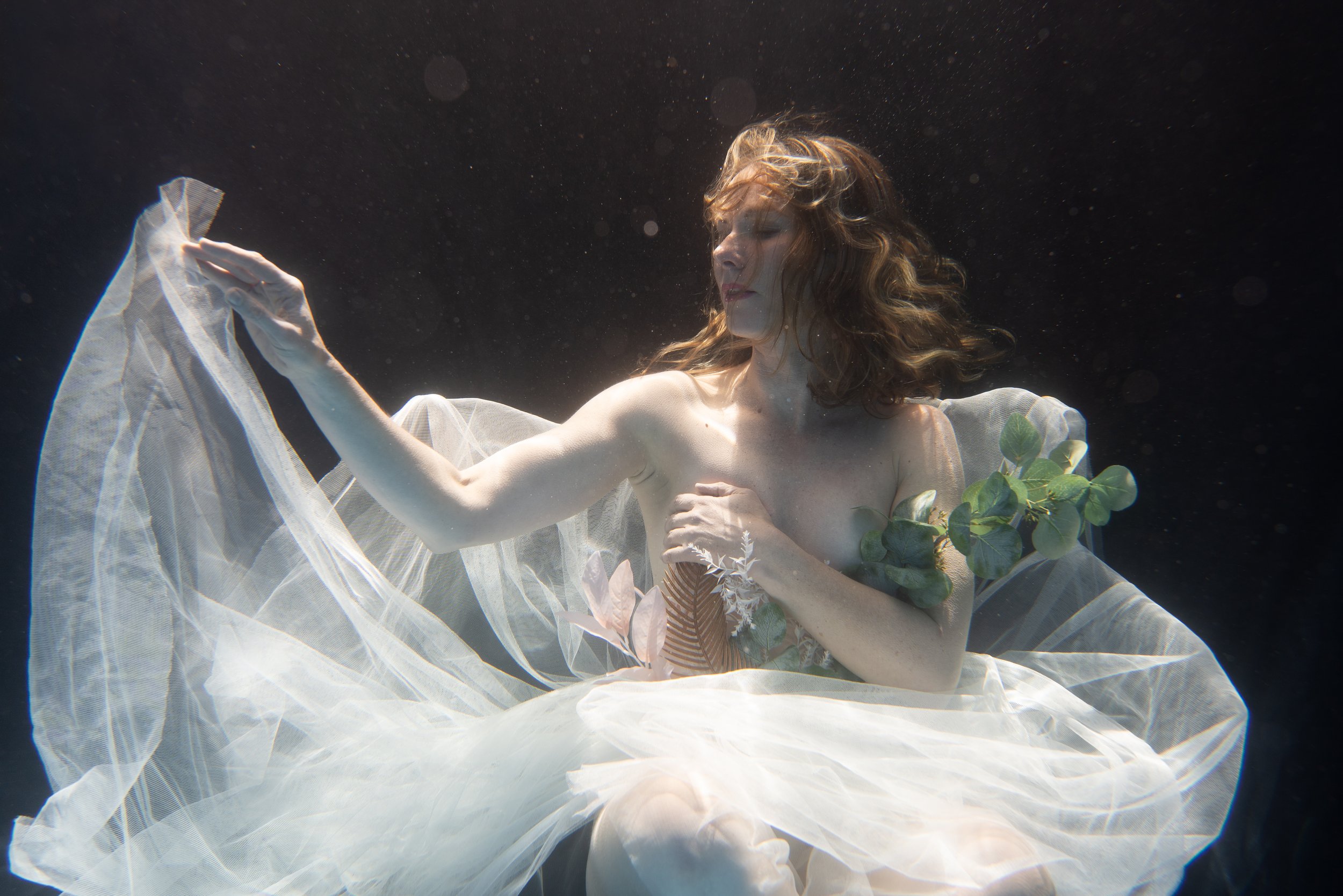 Underwater fine art figure surrounded by flowing translucent tulle and soft cinematic light