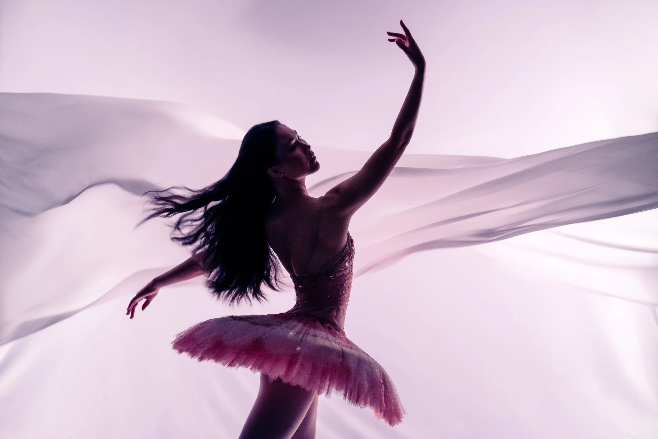 Fine art ballet silhouette with flowing fabric and soft pink light