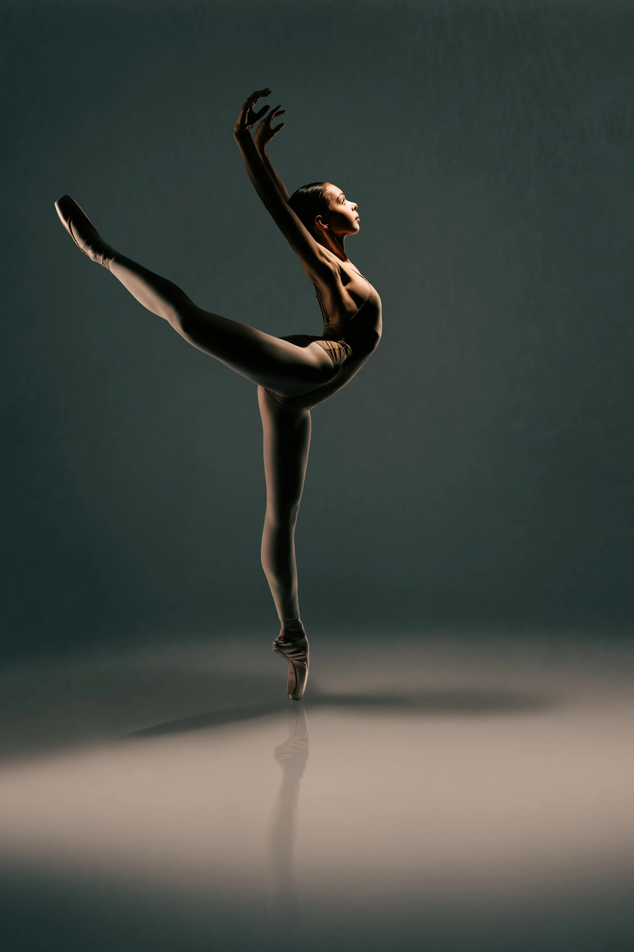 Fine art ballet portrait in arabesque pose with sculptural light and soft shadow