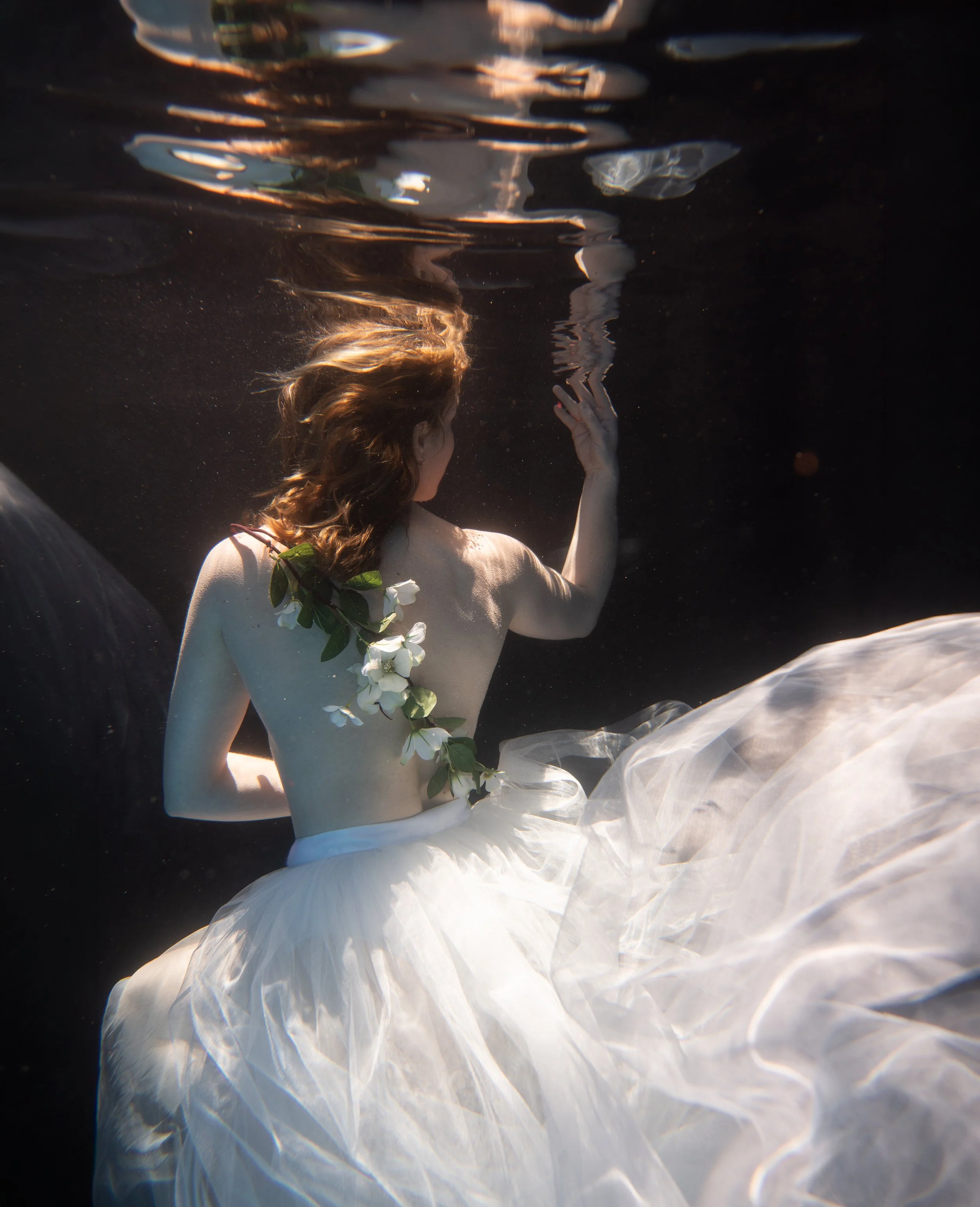 Underwater portrait with flowing white fabric, floral details, and soft cinematic light