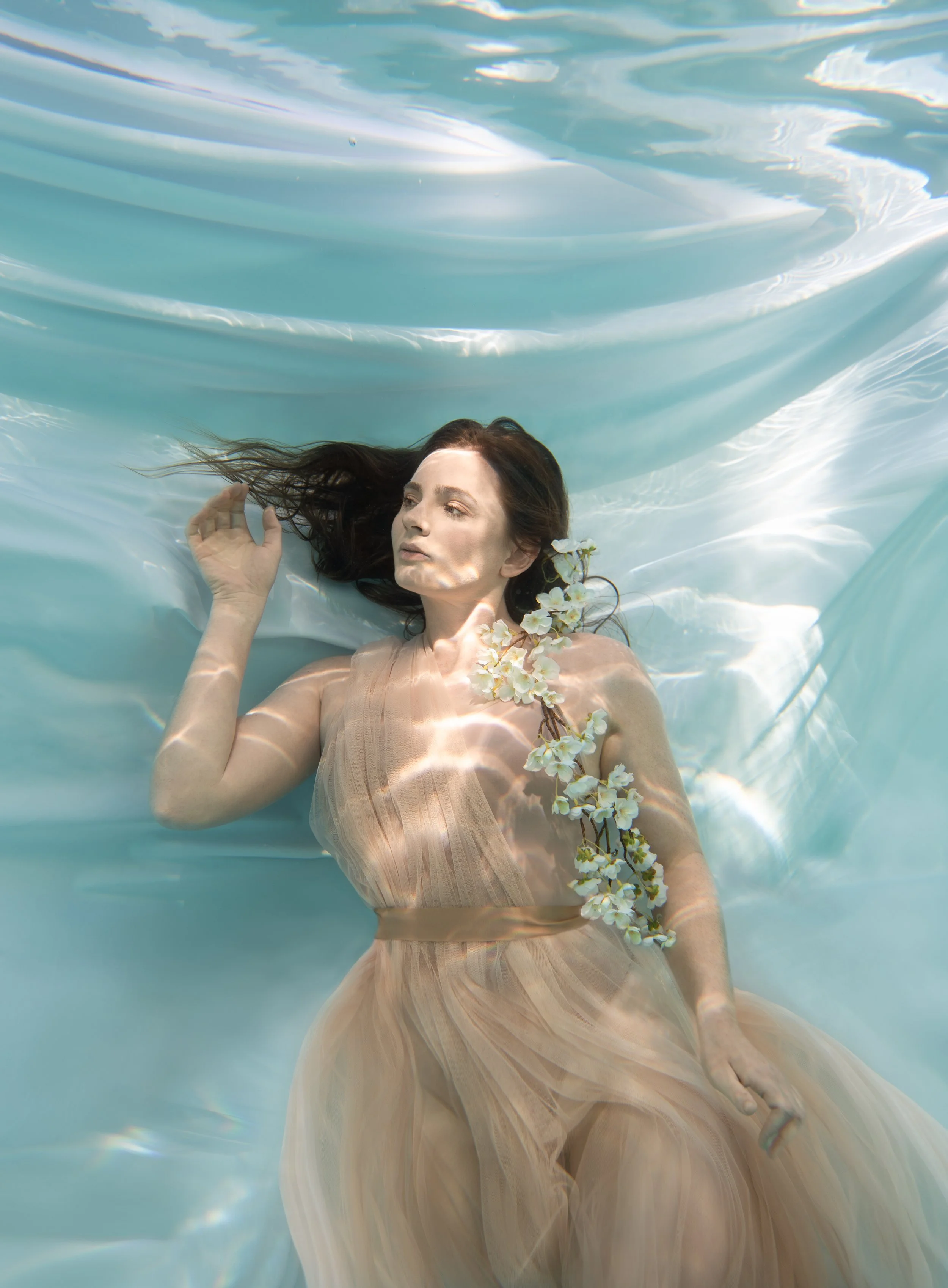 Ethereal underwater portrait with soft floral details and flowing fabric