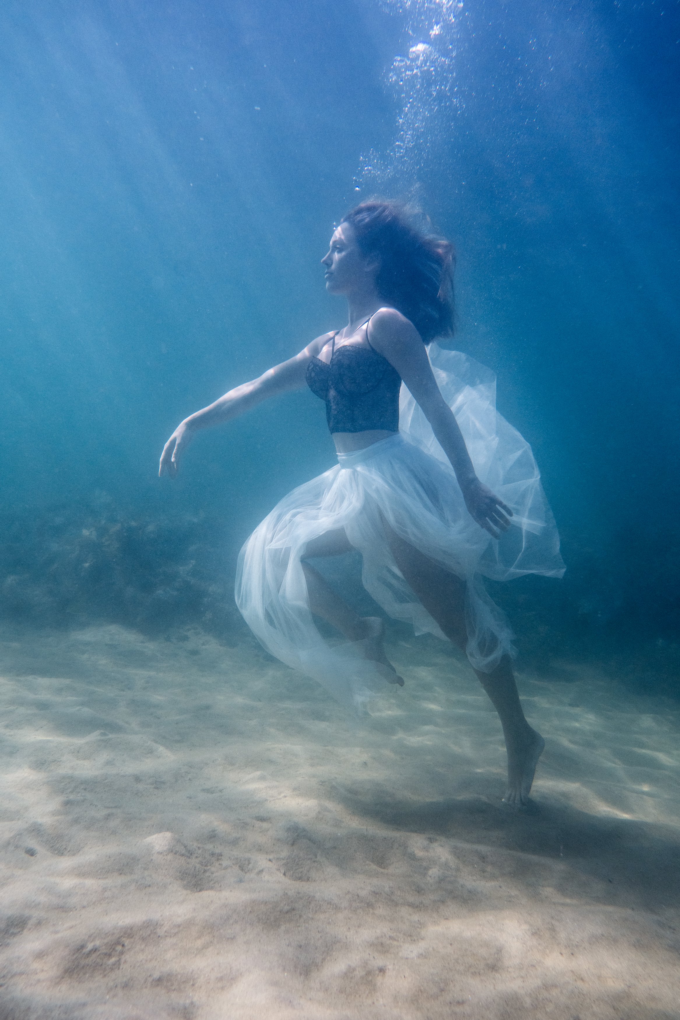 Underwater dancer suspended in soft blue light with flowing tulle skirt