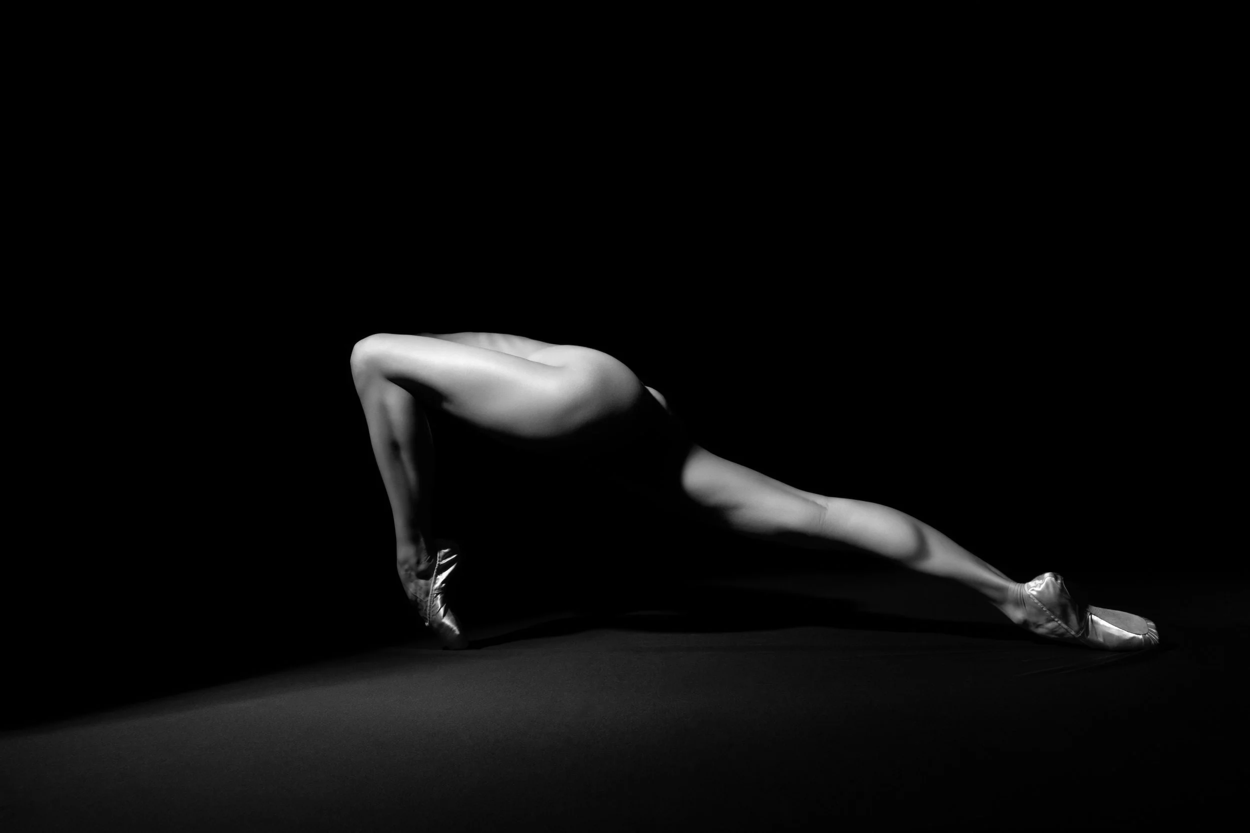 Fine art black and white photograph of an elongated ballet figure extended across darkness