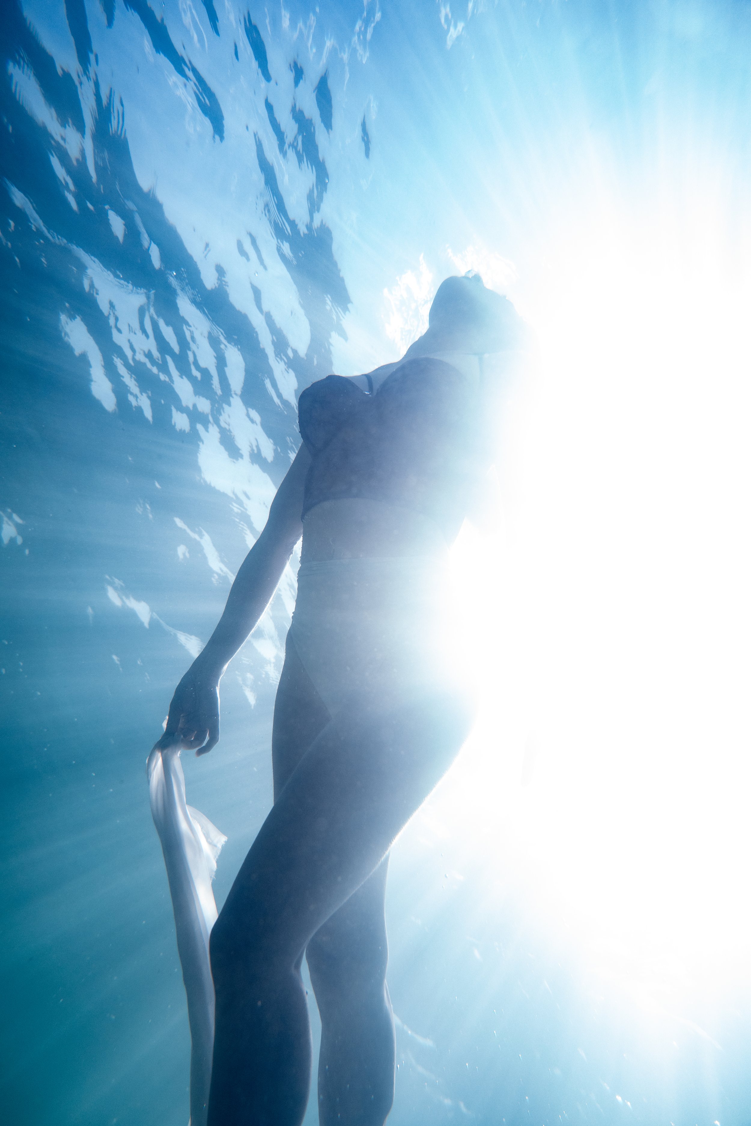 Underwater silhouette portrait with flowing fabric and cinematic rays of light