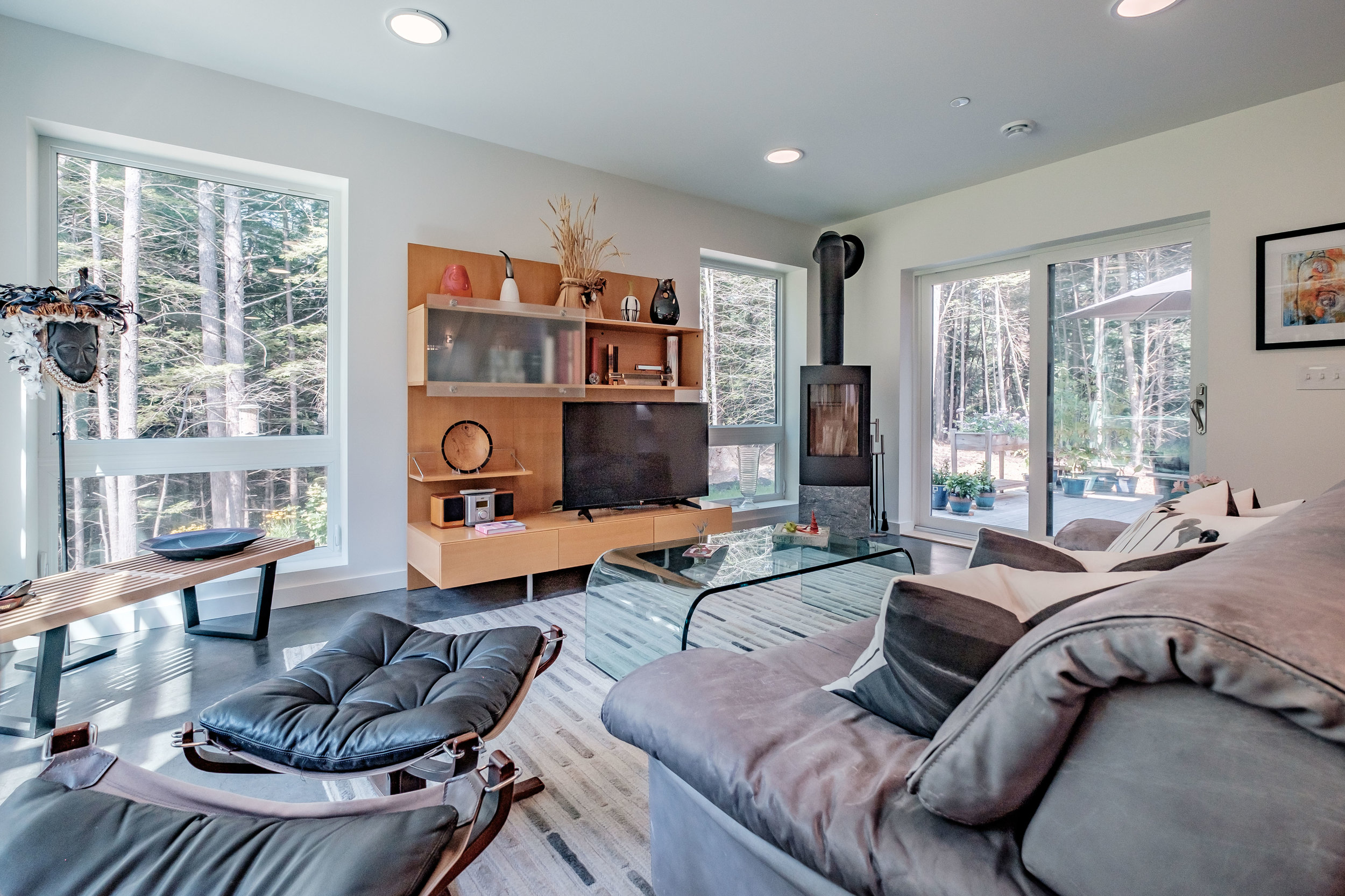 Interior of Kelsey Brook's newest home—designed by Mottram Architecture— showing the Tula wood stove that was central to its design. Triple pane windows face west to oer shading from the summer sun and sit just above the floor, giving the appearance of being connected to the woods beyond. Photo: Michael Eric Berube