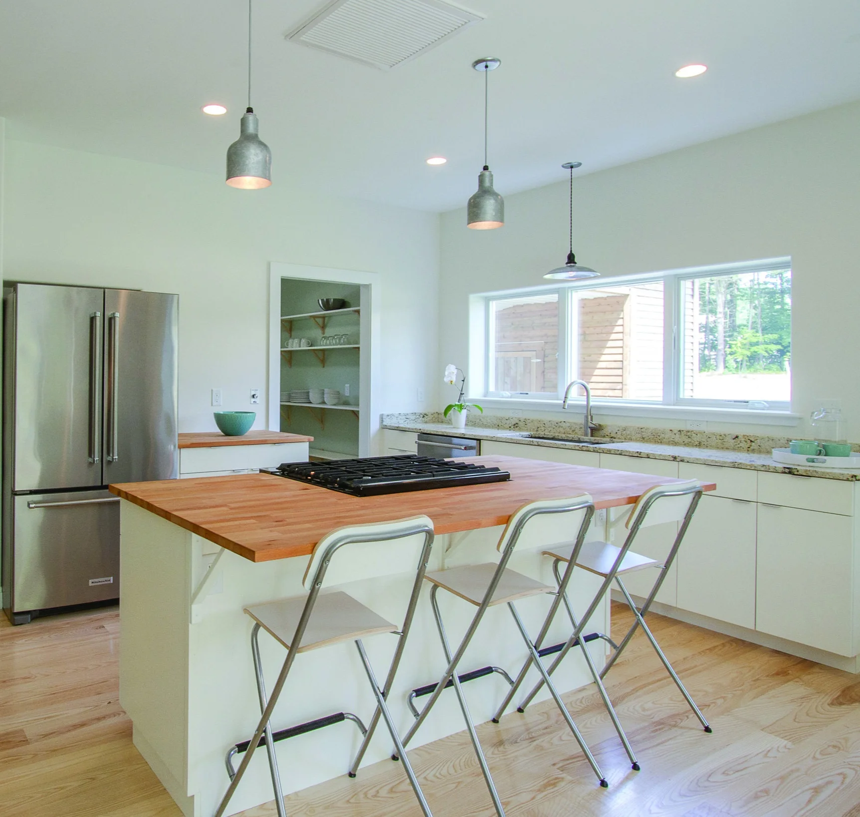 Locally-built custom cabinetry combined with an oversized walk-in pantry creates ample storage opportunities while maintaining the open feel and clean lines by avoiding upper cabinetry. The combination of stone and butcher block counter tops adds texture and appeal.