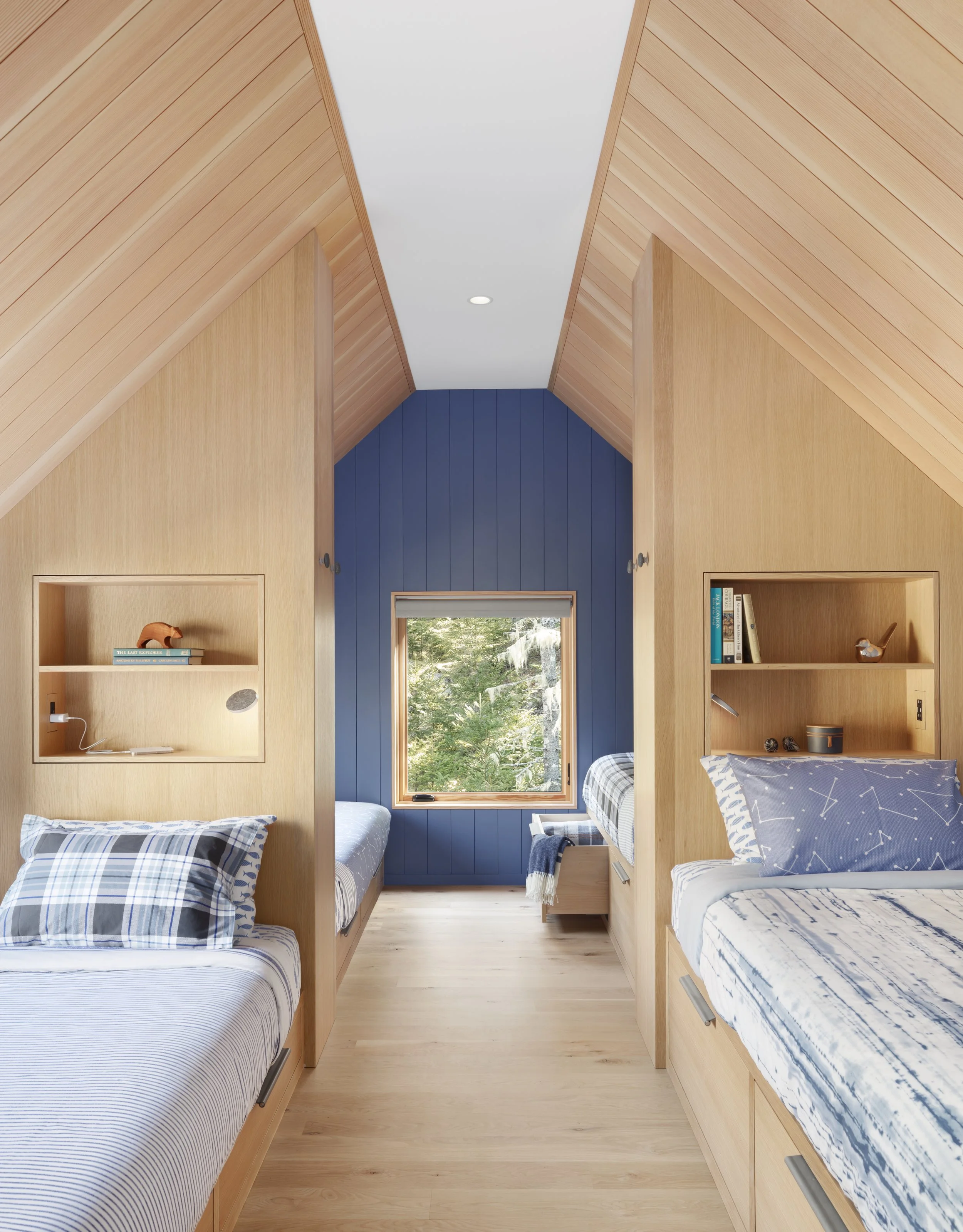  With beautifully finished light wood everywhere, large windows and a pop of deep blue on the far wall, the bunkroom is a welcoming retreat for lucky guests. It's also a study in functional detail: The two sets of captain’s beds are divided by floor-