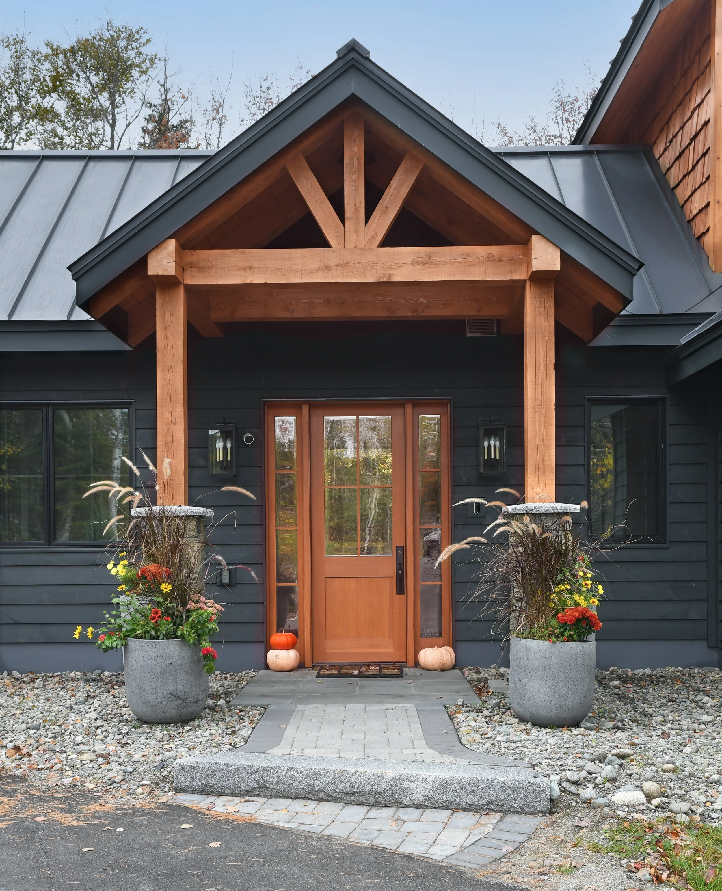 The home entryway is framed by two large stone planters, a stone path, and a wooden door that stands out against the dark wood siding.