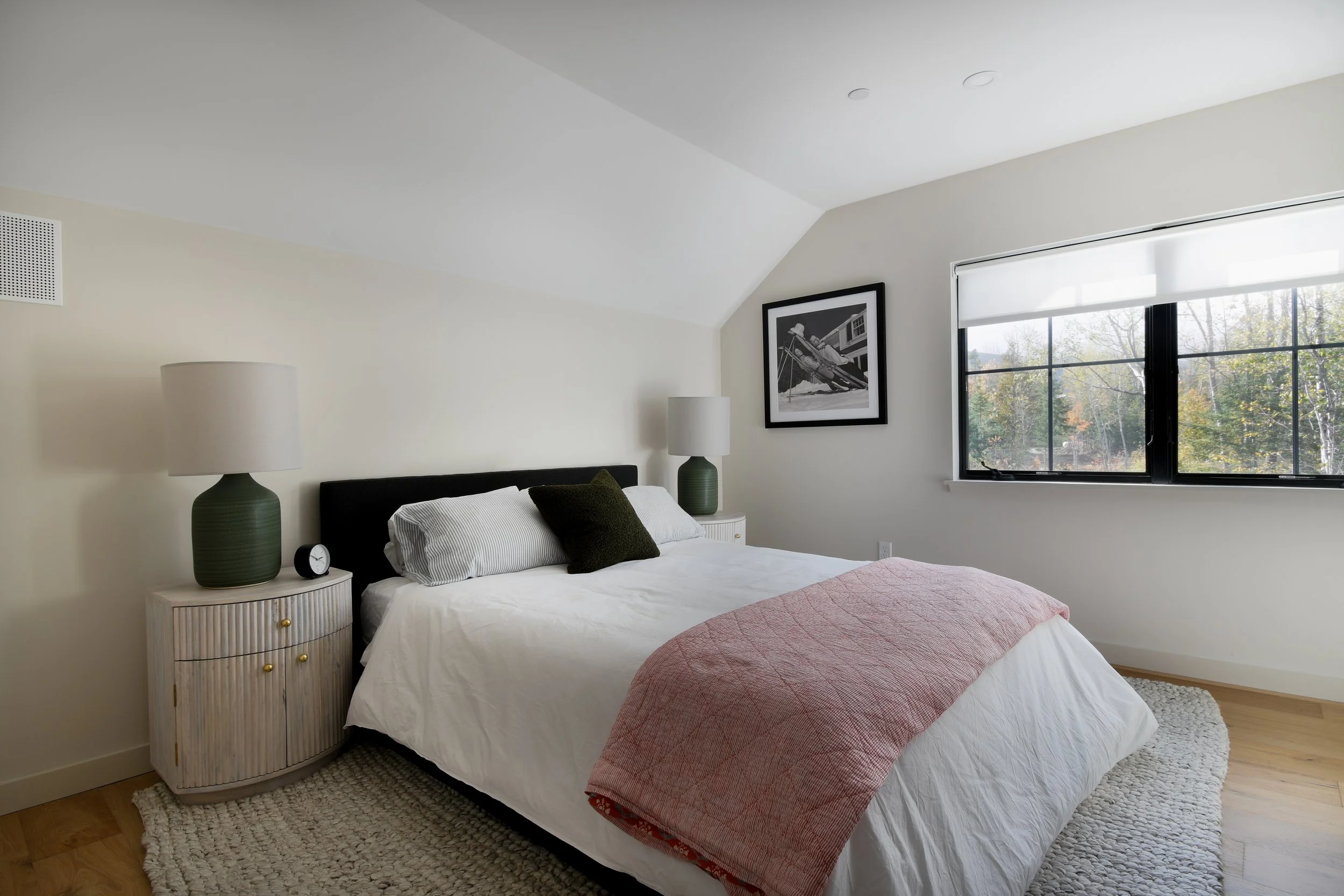 A bedroom with a minimalist color palette and a pop of color with a pink blanket.