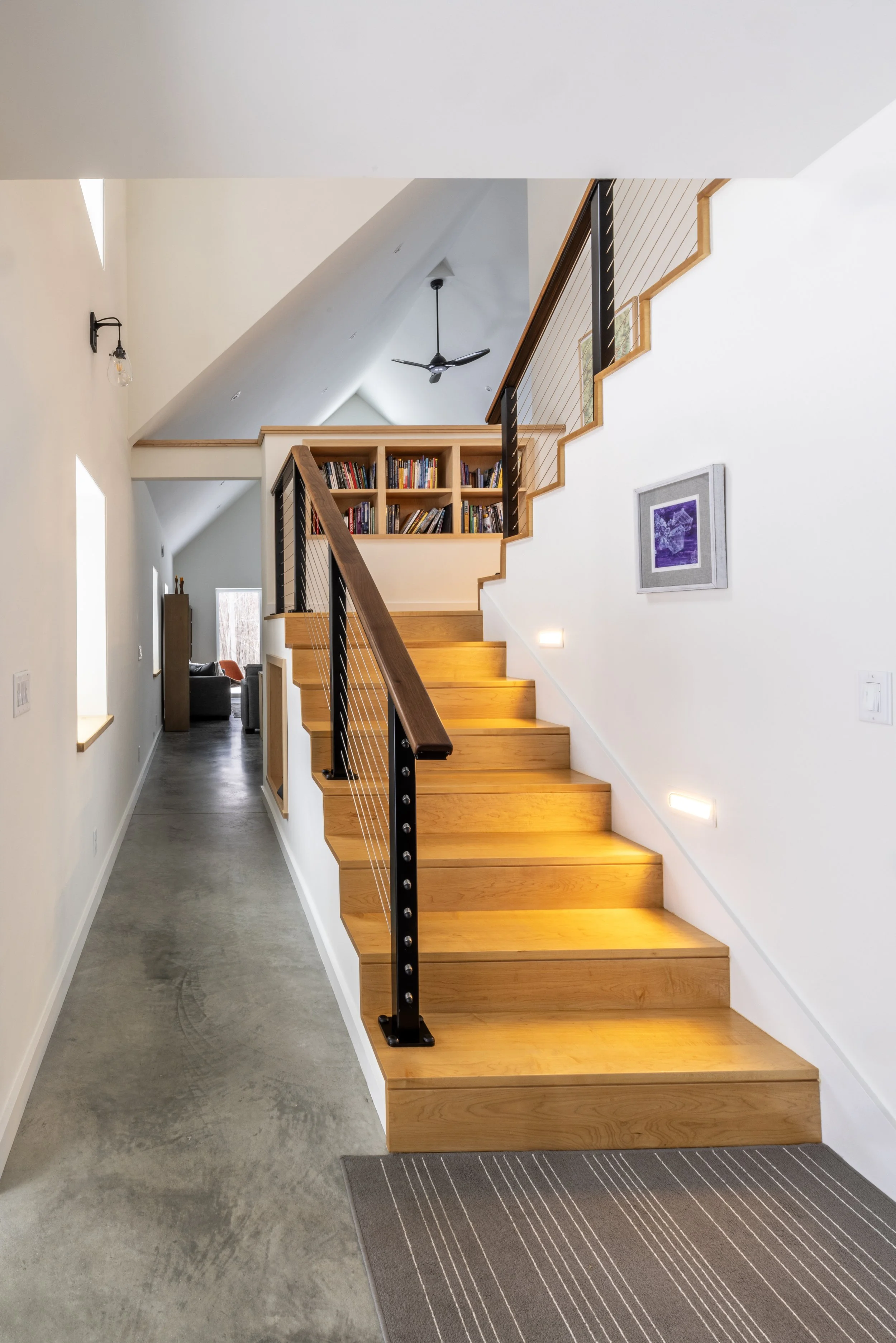 A staircase with warm wooden tones has a built in bookcase halfway up, on the landing.