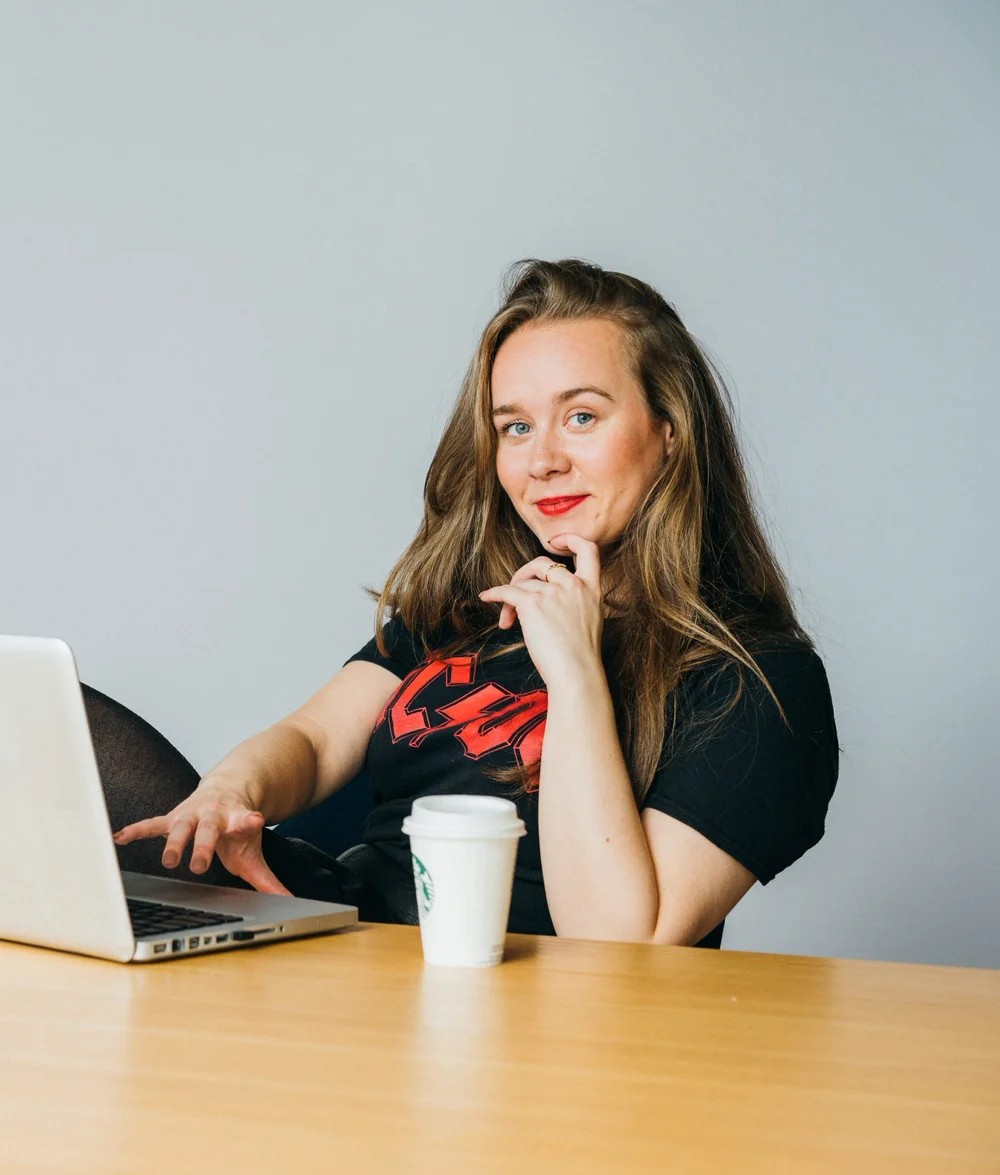 Nic Moors smiling, hands on hips, in a black band T-shirt and leather skirt